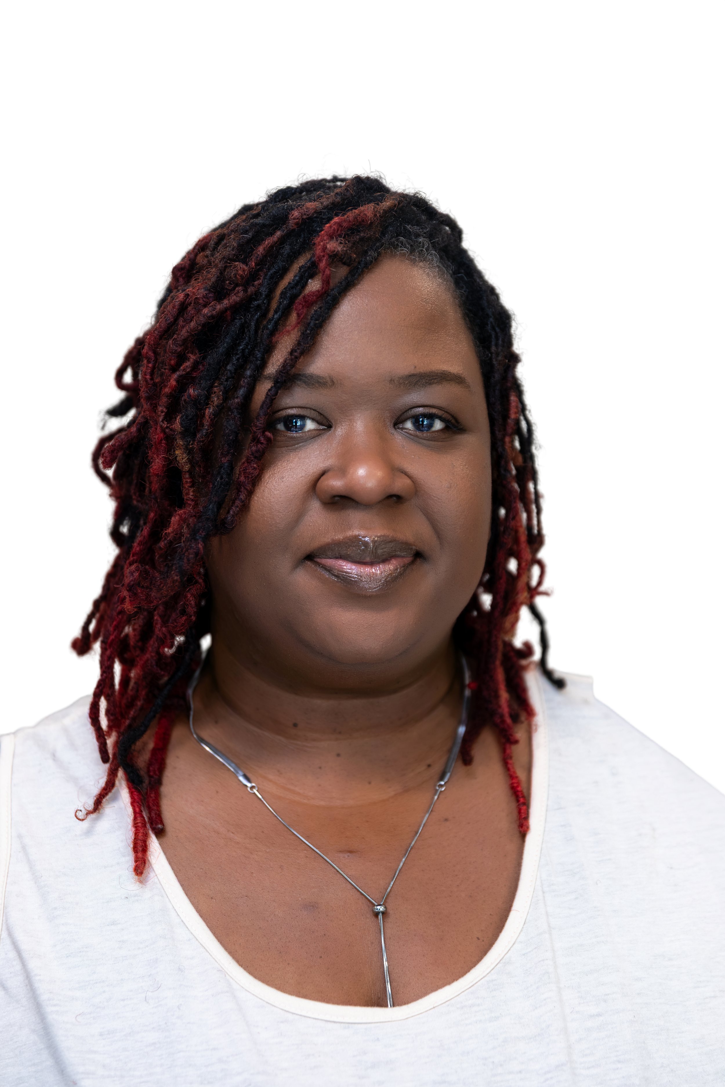 Portrait of a woman with short hair and purple dreadlocks, smiling, wearing a white shirt, against a plain background.