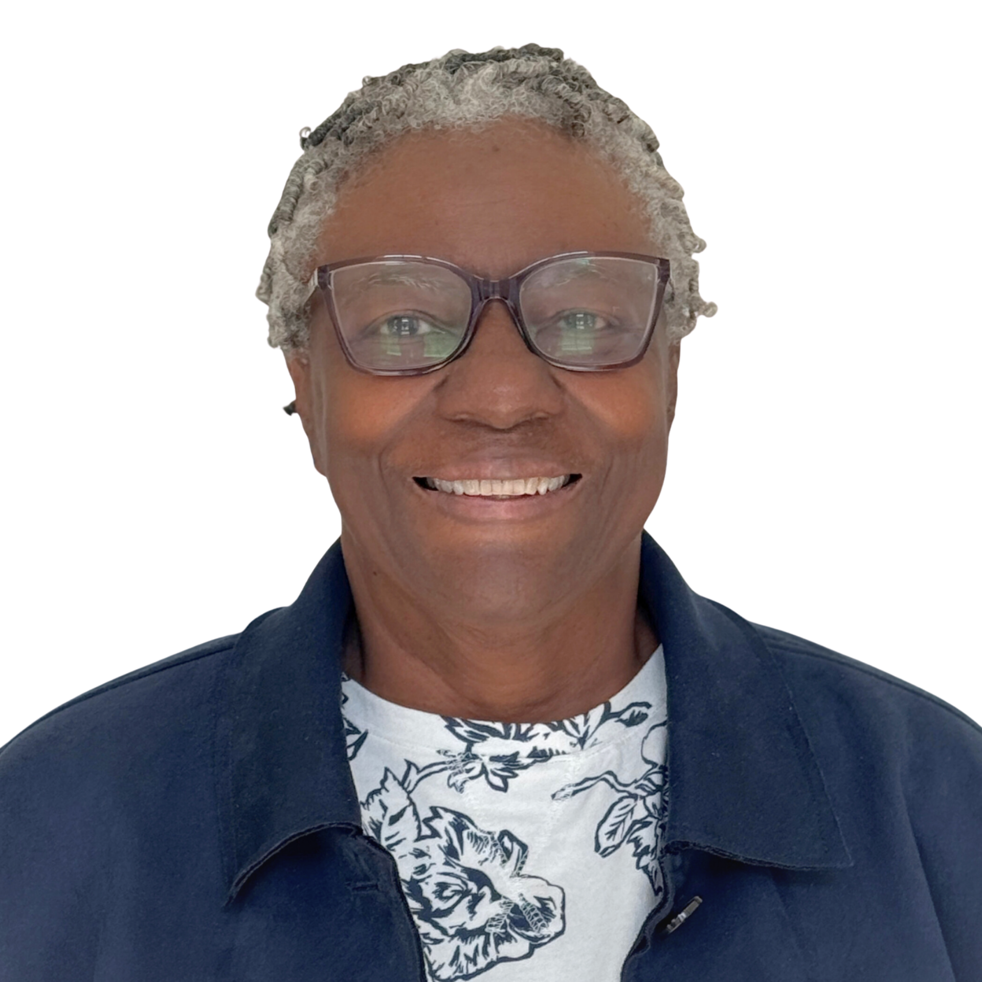 Smiling woman with gray twisted hair, wearing glasses, large blue earrings, a dark jacket, and a white shirt with black leaf print, standing against a plain light background.