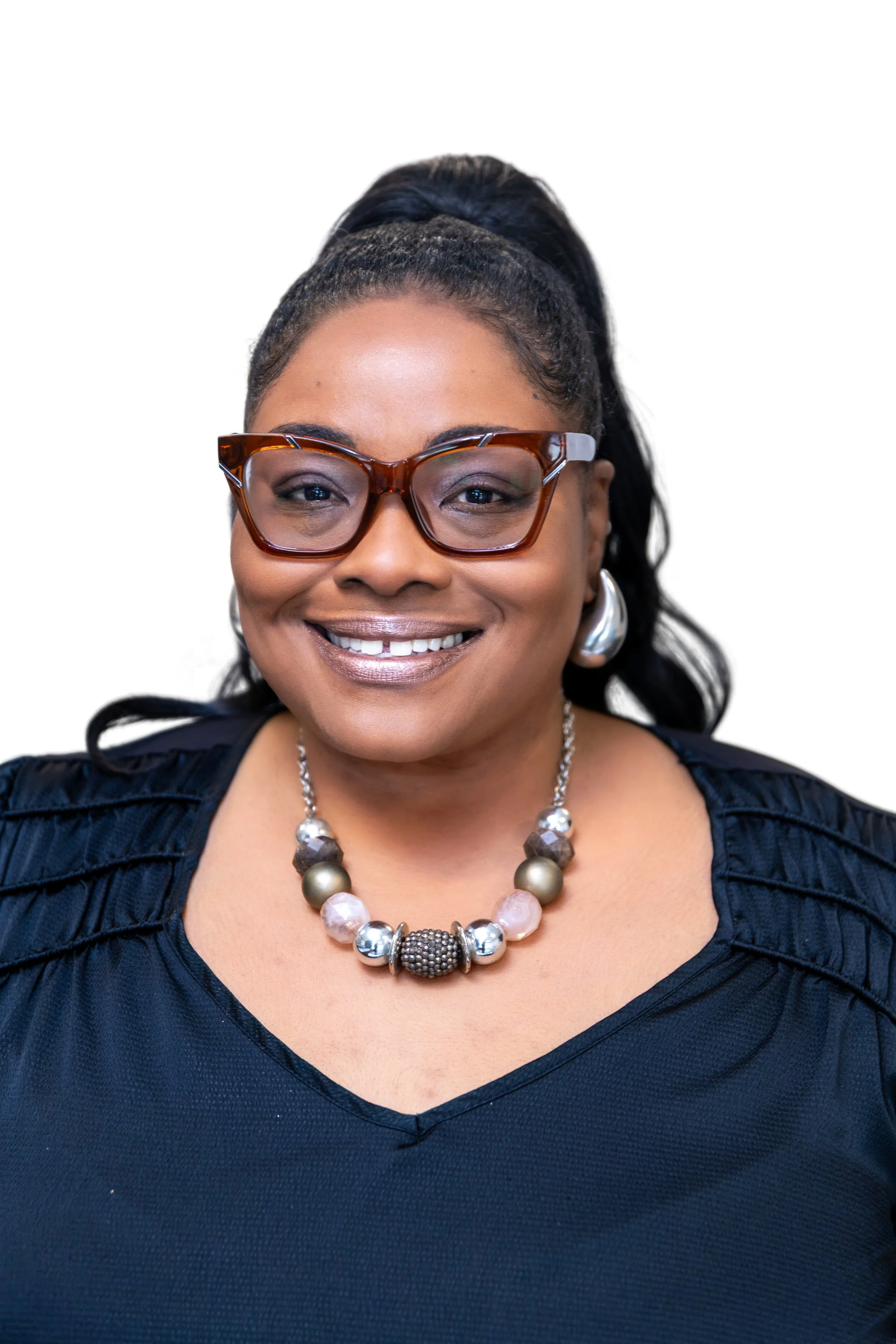 Close-up of a smiling African American woman with braided hair styled in an updo, wearing a green sweater and earrings, against a plain light-colored background.