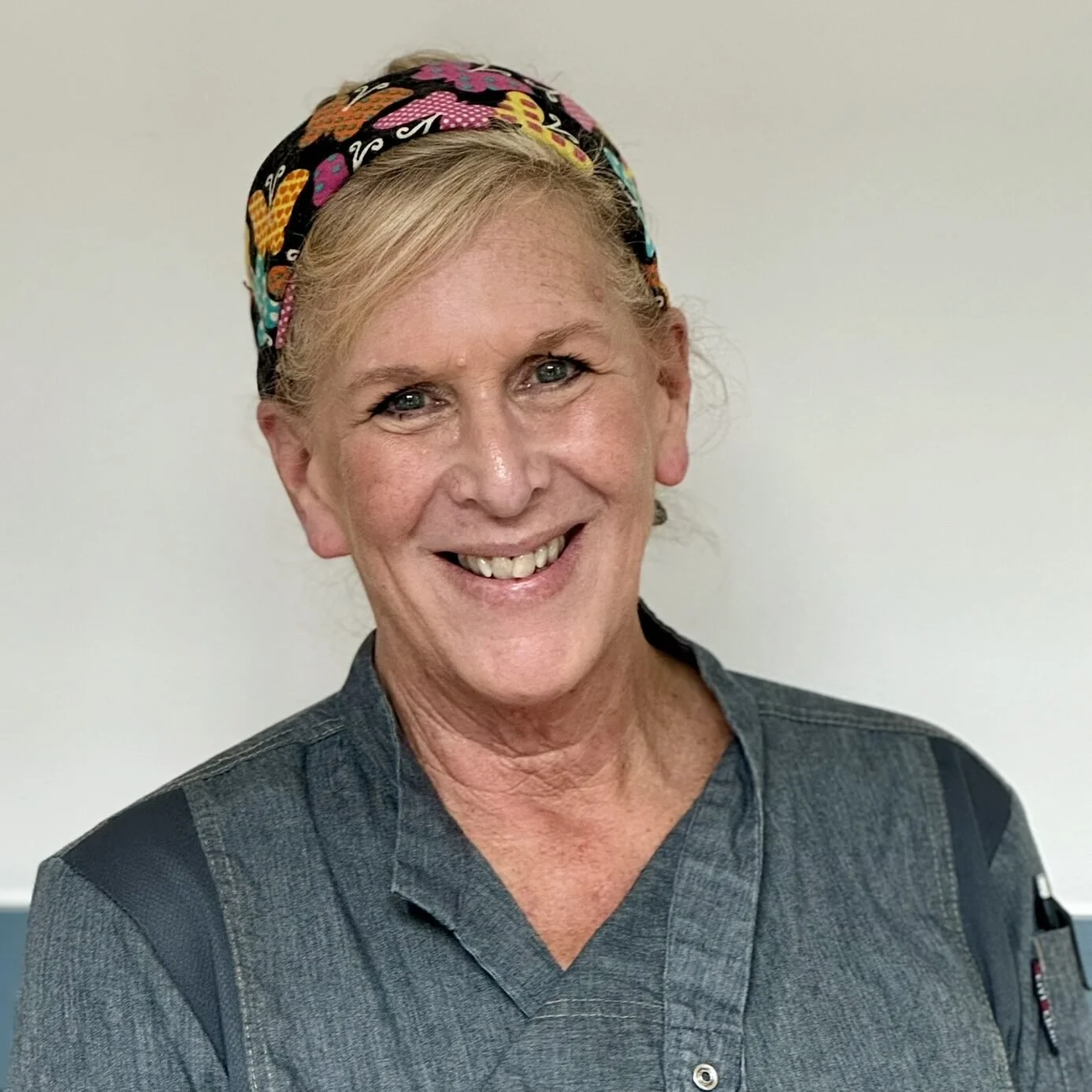 A smiling woman with blue eyes wearing a colorful headscarf and a gray uniform with black accents.