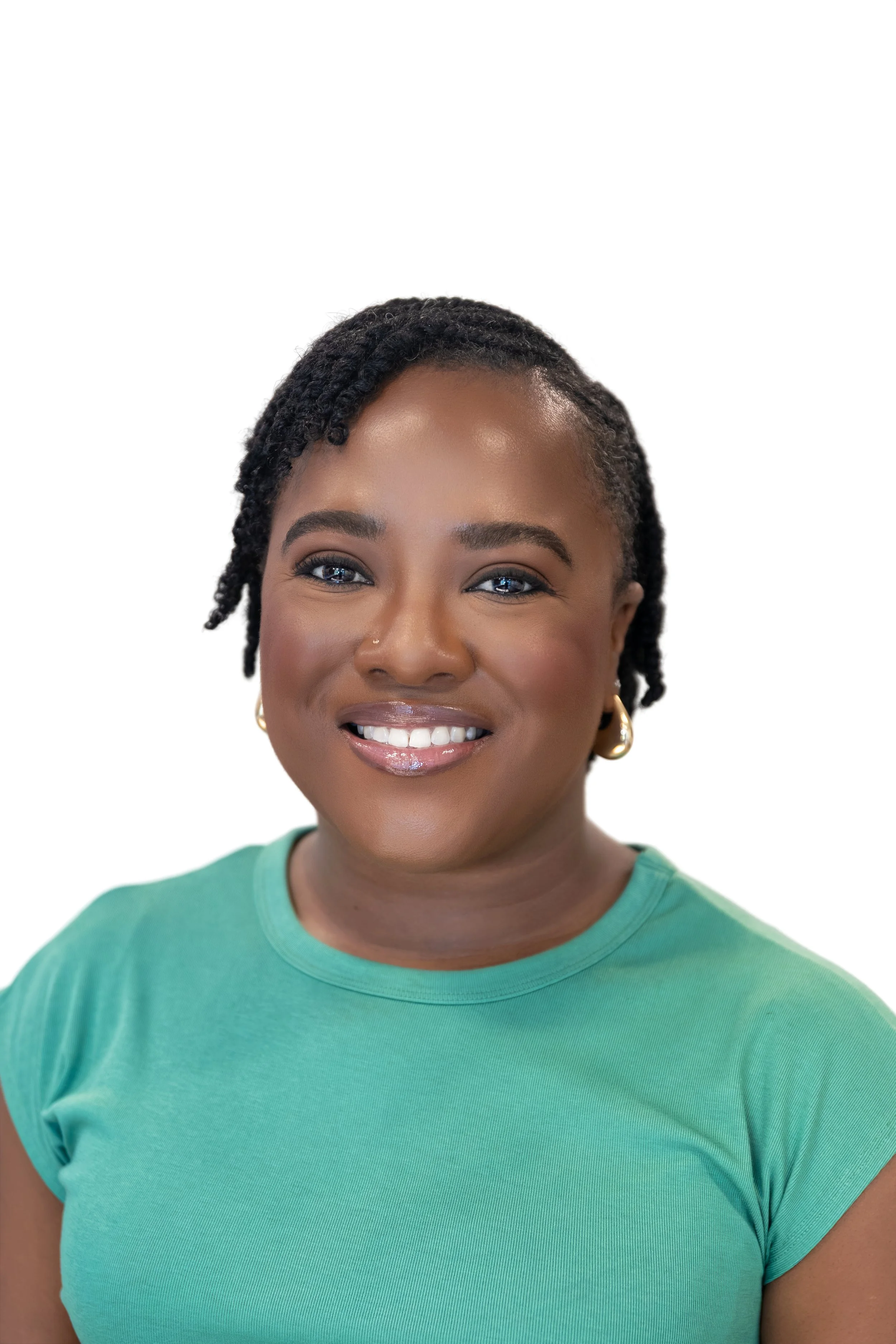 A woman with brown skin and blonde dreadlocks styled in a high bun, wearing a light blue denim shirt and gold hoop earrings, smiling at the camera.