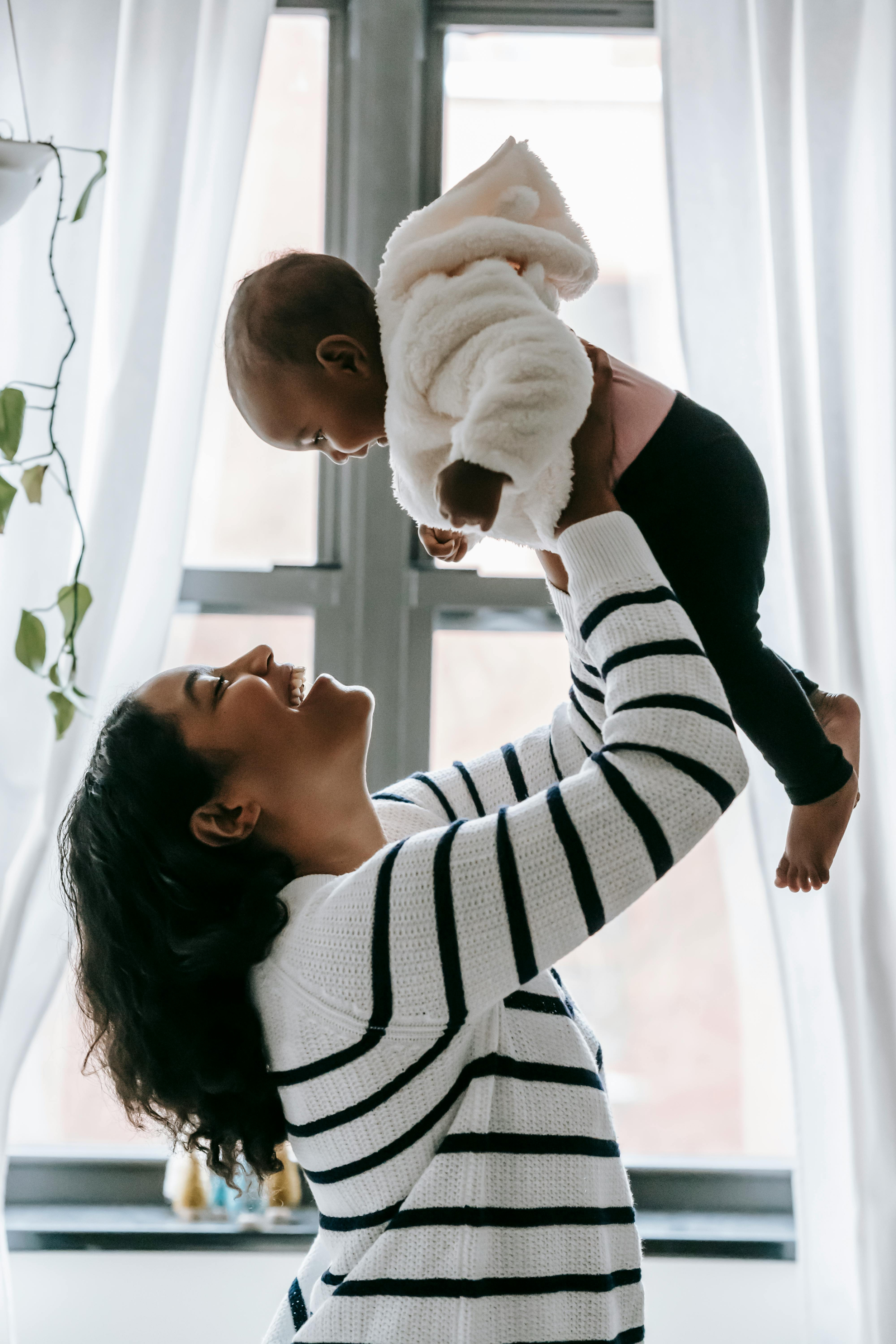 A young mother lifts her child with a smile, reflecting the joy and stability fostered through Sarah's House.