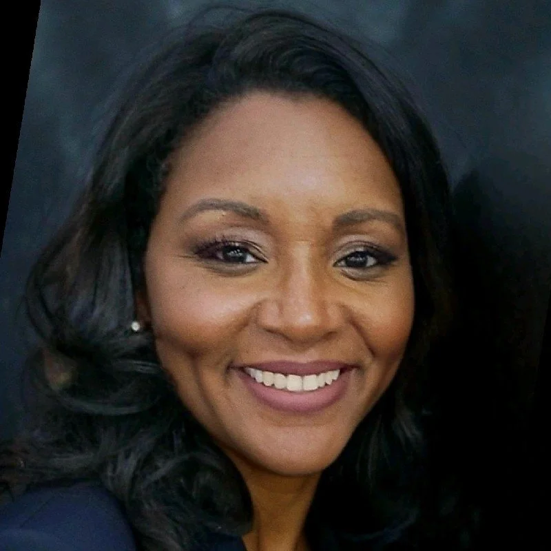 A smiling woman with dark hair and pearl earrings, against a dark background.