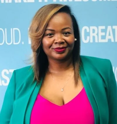 A woman with shoulder-length hair, wearing a teal blazer over a pink top, standing in front of a blue background with white text.