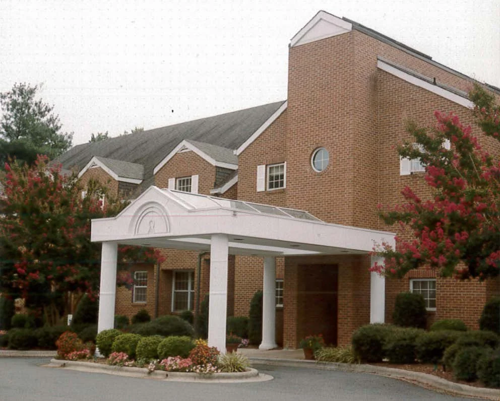 Brick building with a white portico, surrounded by landscaped bushes and flowering trees.
