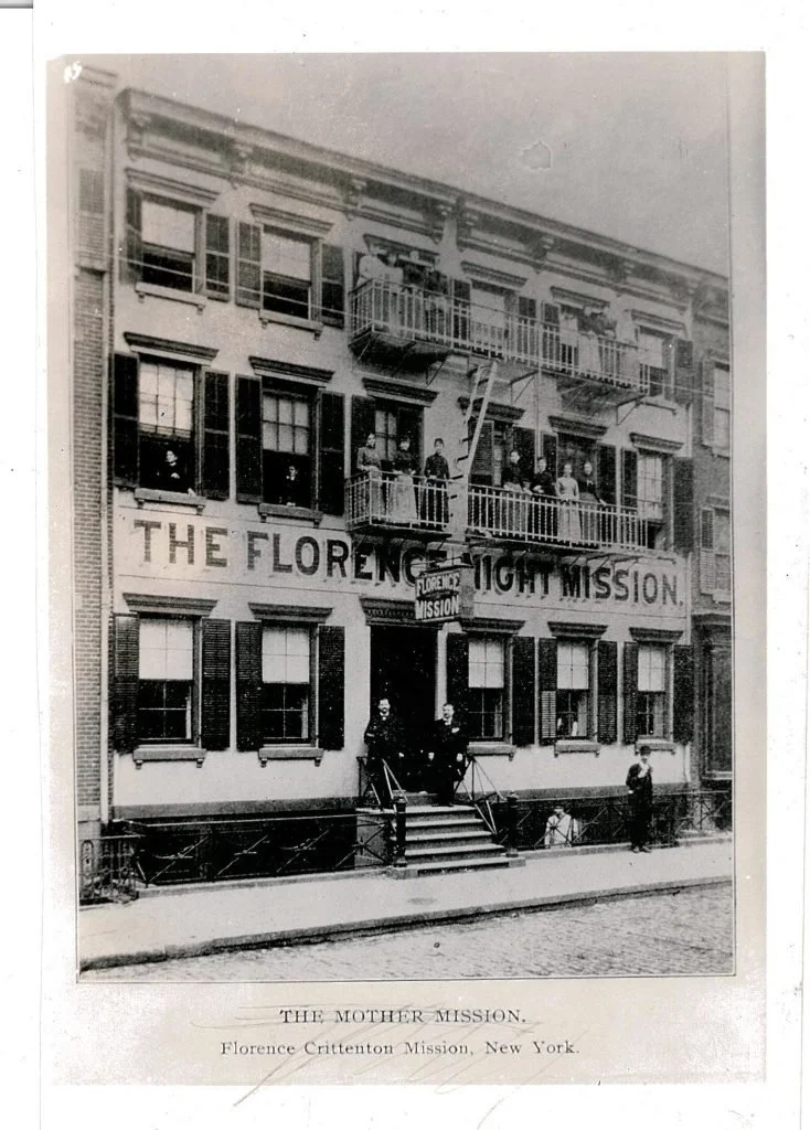 Historical black and white photo of a three-story building with a sign reading "The Florence Night Mission." People stand on multiple balconies and in front of the entrance, which has stairs leading up to it. The building is located in New York, as indicated by the caption.