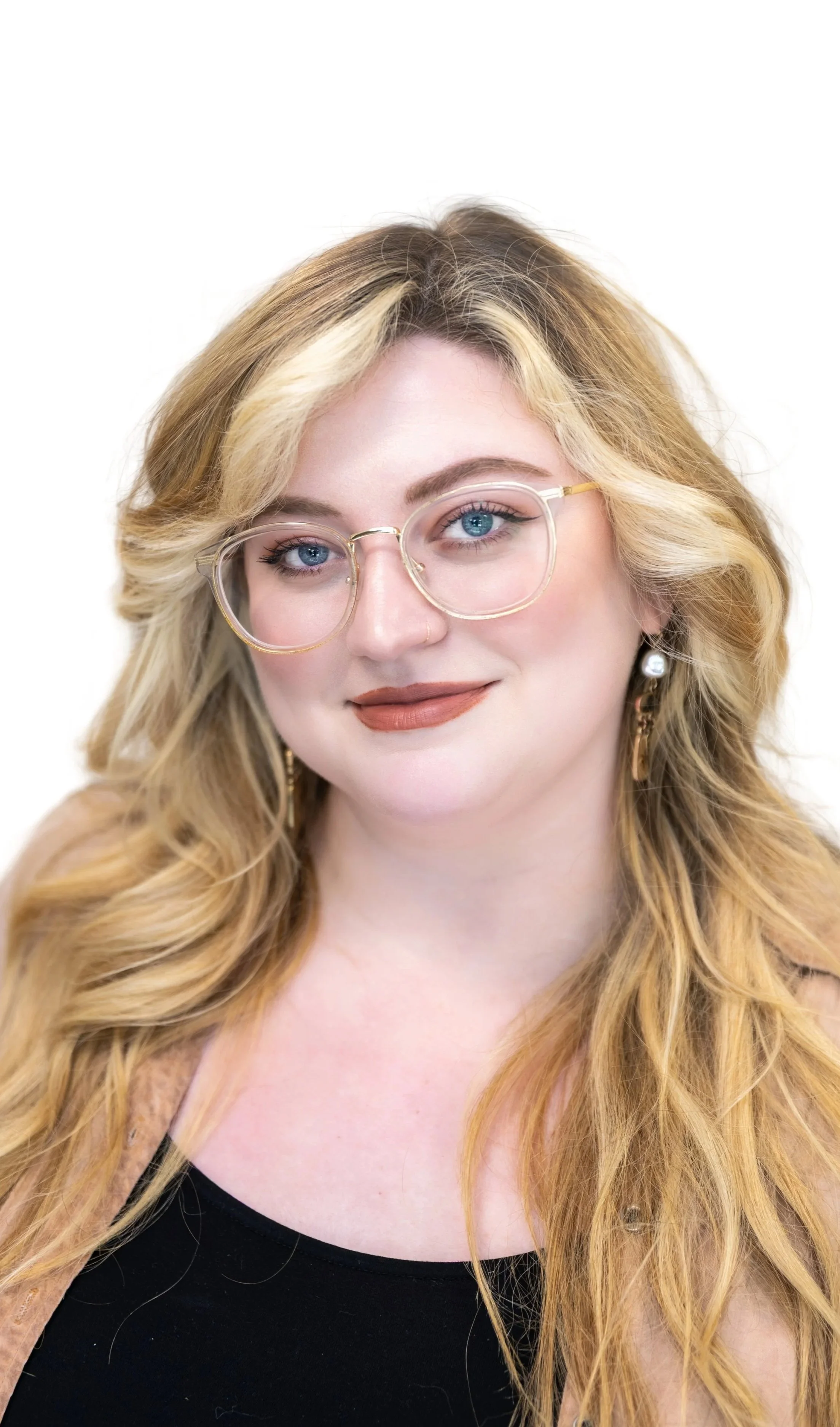 A woman with long blonde hair, glasses, and a black top smiling against a plain light-colored background.