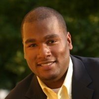 Portrait of a young man in a suit outside with greenery in the background.