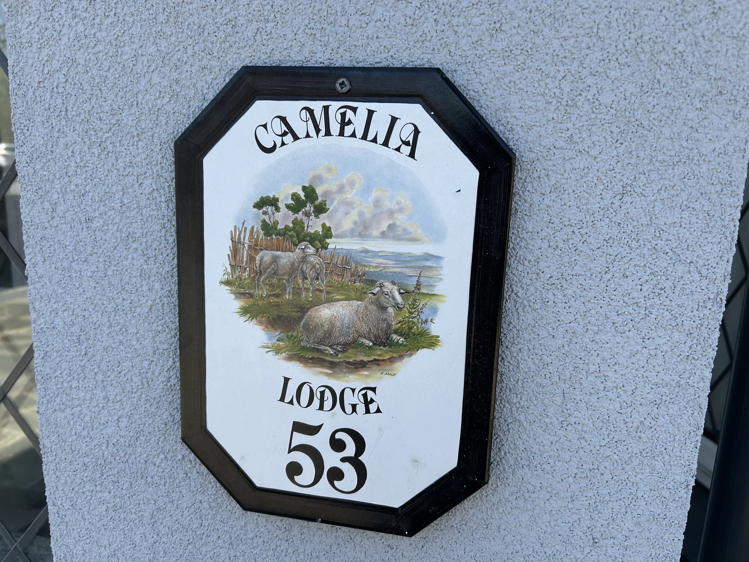 Sign with the word 'CAMILIA' at the top, featuring a watercolor illustration of sheep, trees, and a landscape, and displaying the text 'LODGE 53' at the bottom.