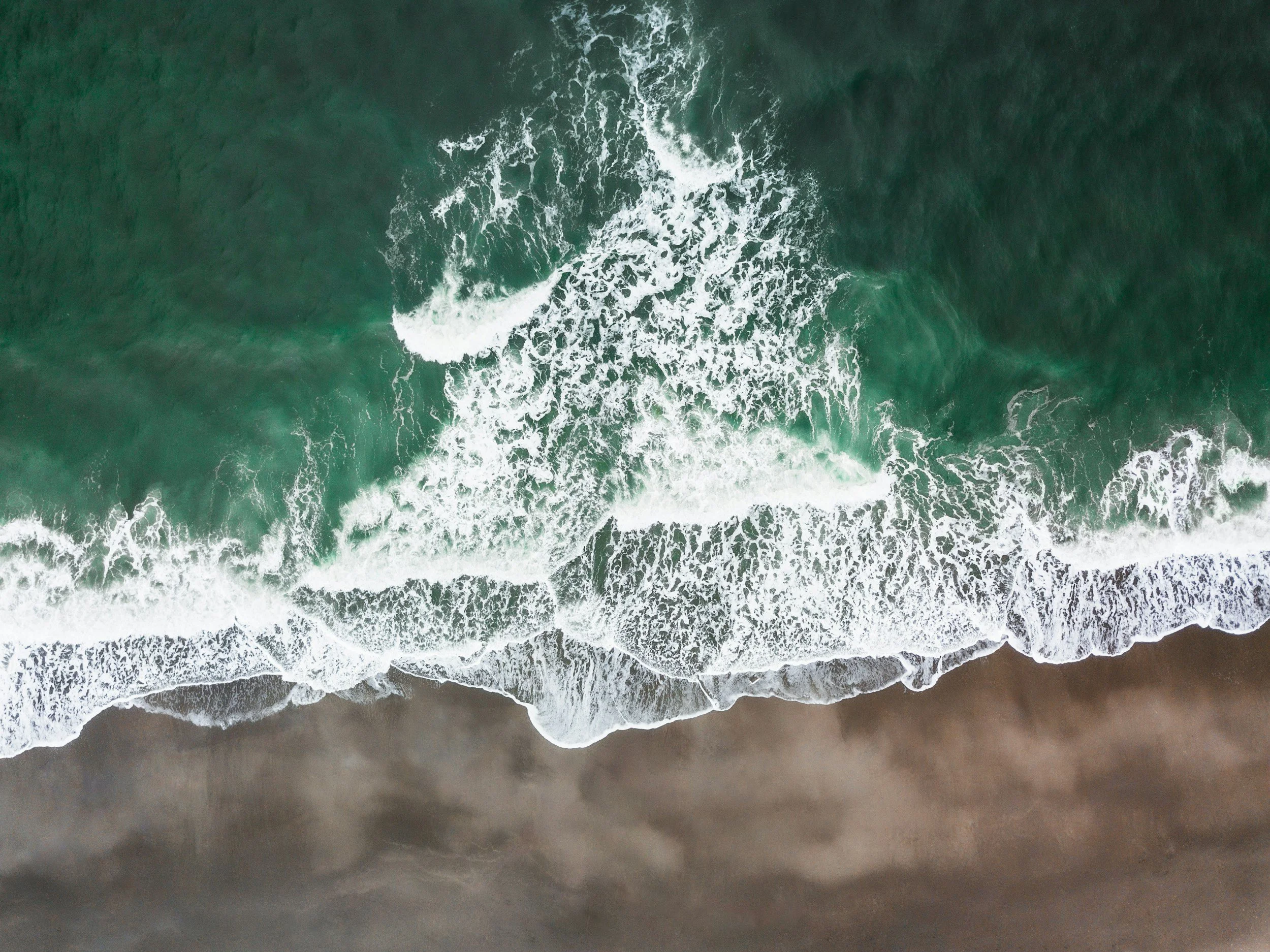 Aerial view of green ocean waves crashing onto sandy beach.
