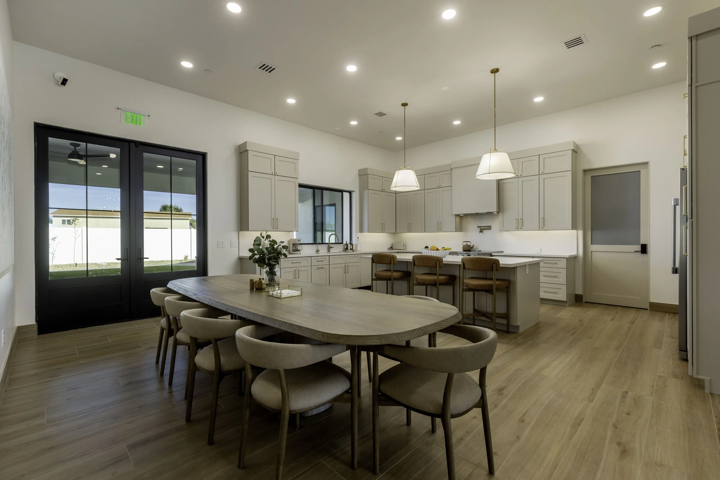 Open-concept kitchen and dining area with light-colored cabinets, pendant lighting, wood flooring, and sliding glass doors.