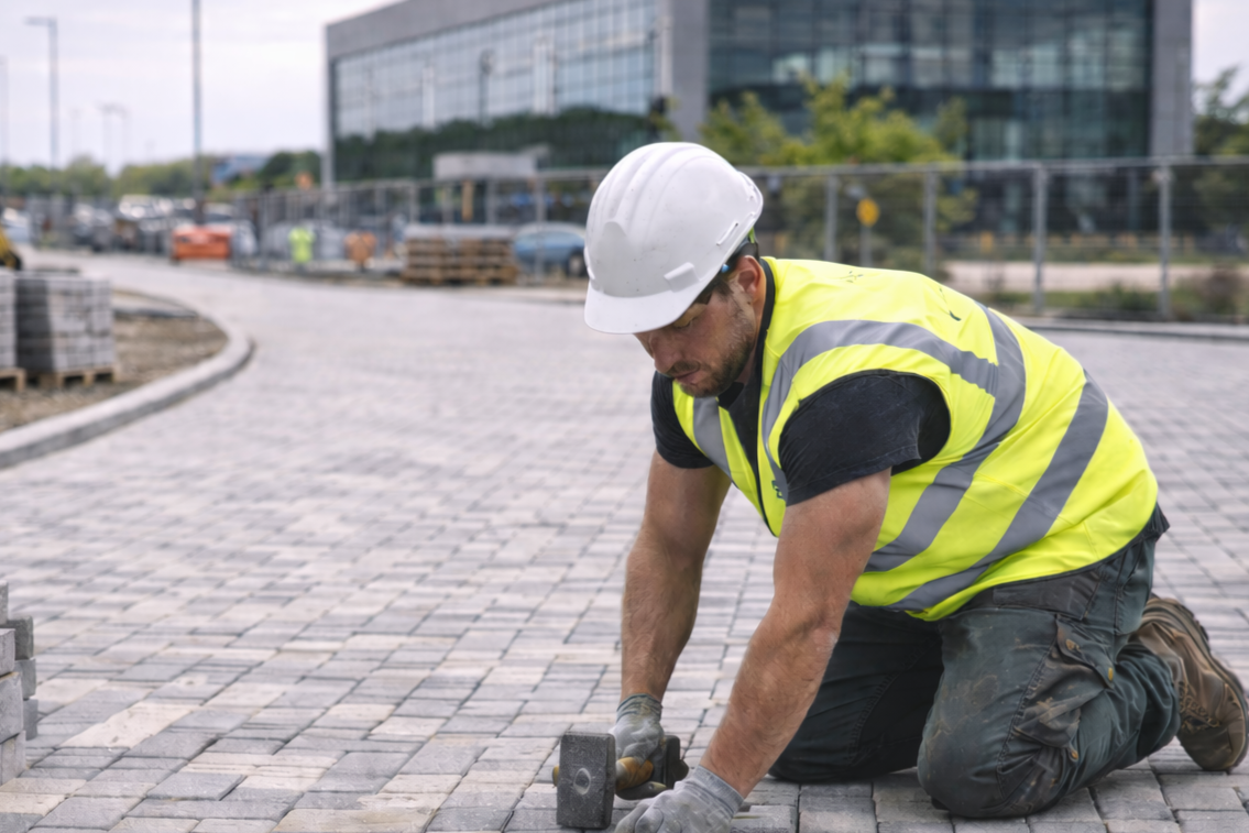 Construction worker kneeling on ground laying block paving stones.