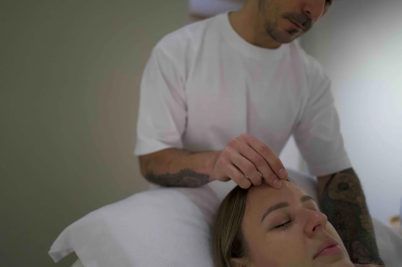 A man giving a facial massage to a woman with her eyes closed in a clinical or spa setting.