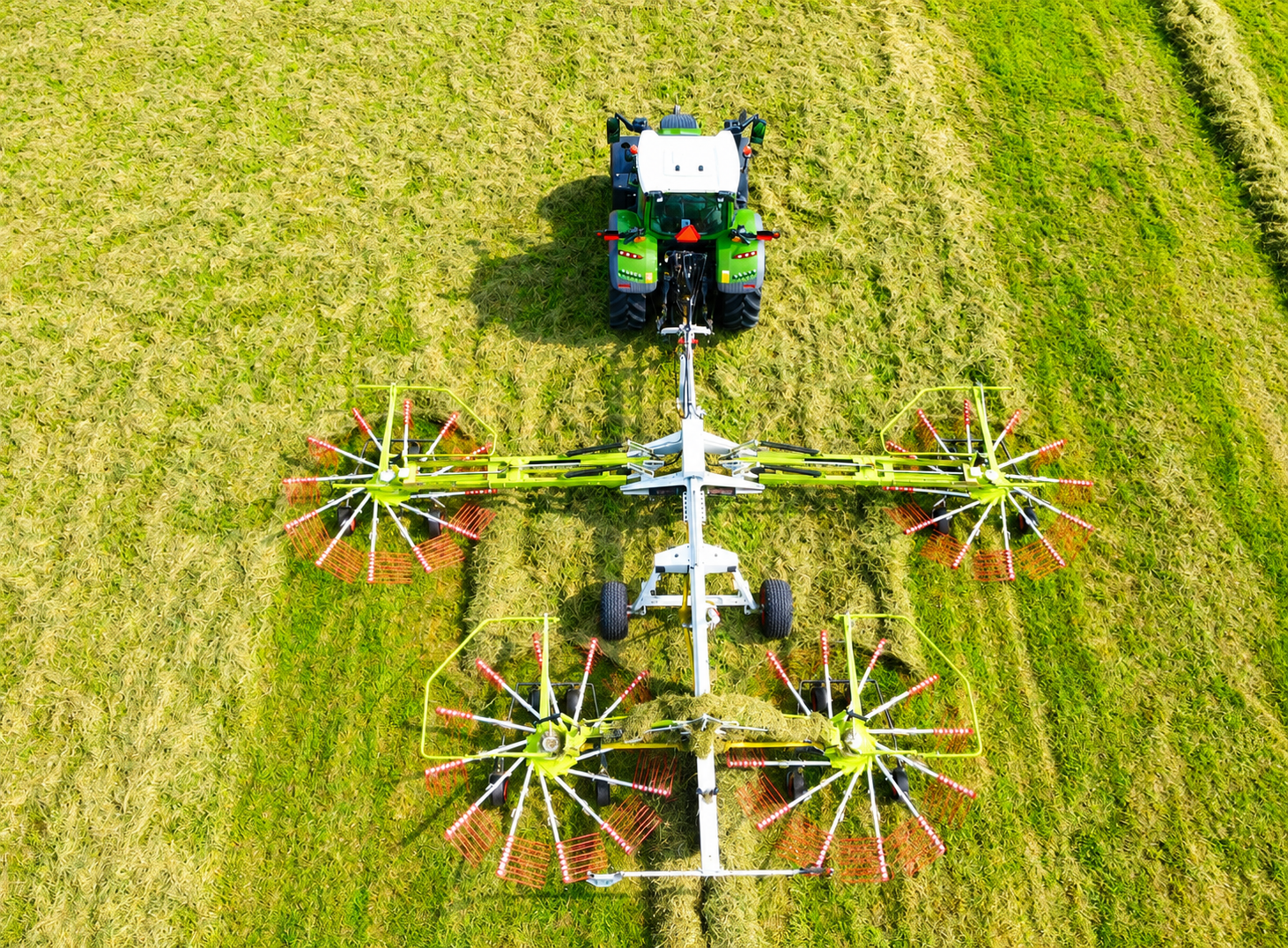 Top-down view of a tractor pulling a large agricultural reel mower across a green field.