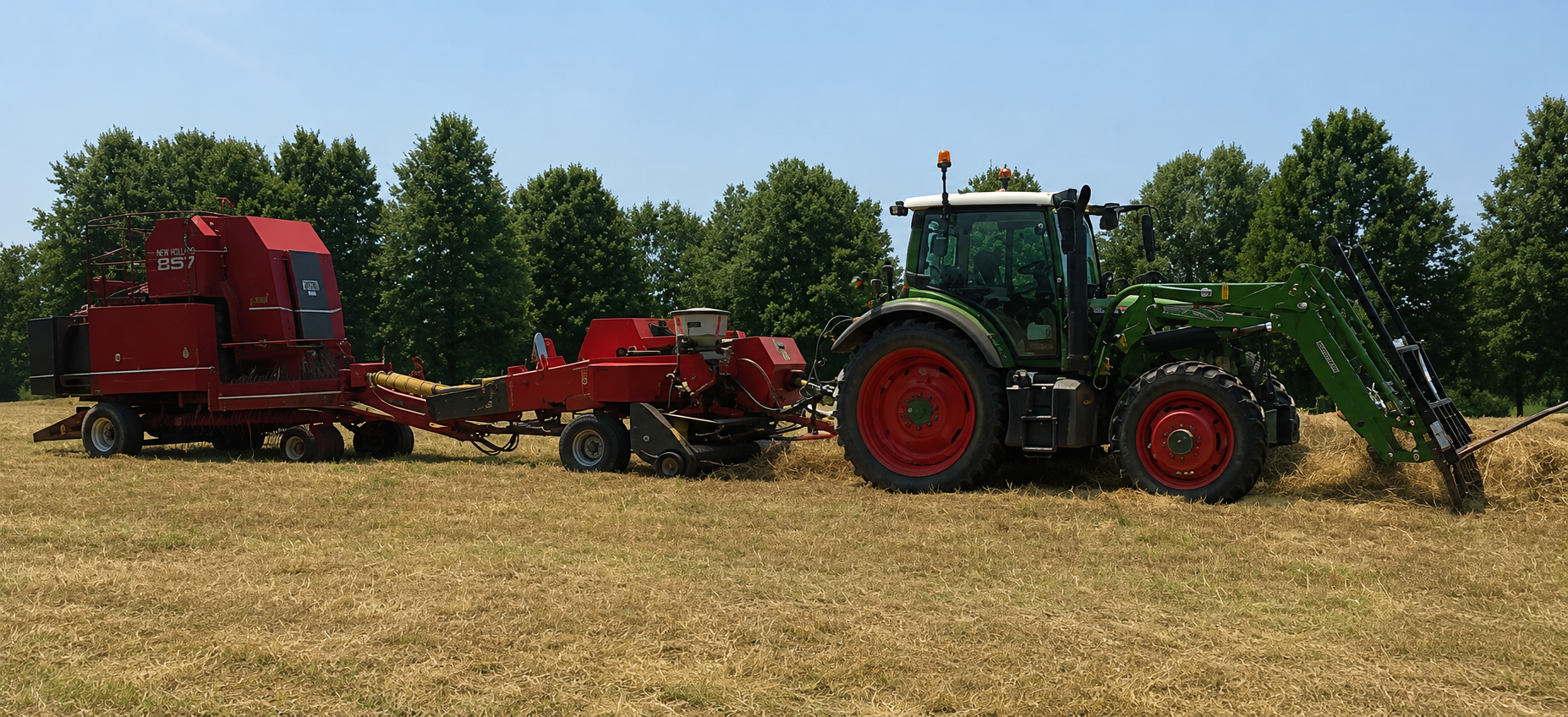 A green and black tractor pulling a red harvesting machine across a dry field with green trees in the background under a clear blue sky.