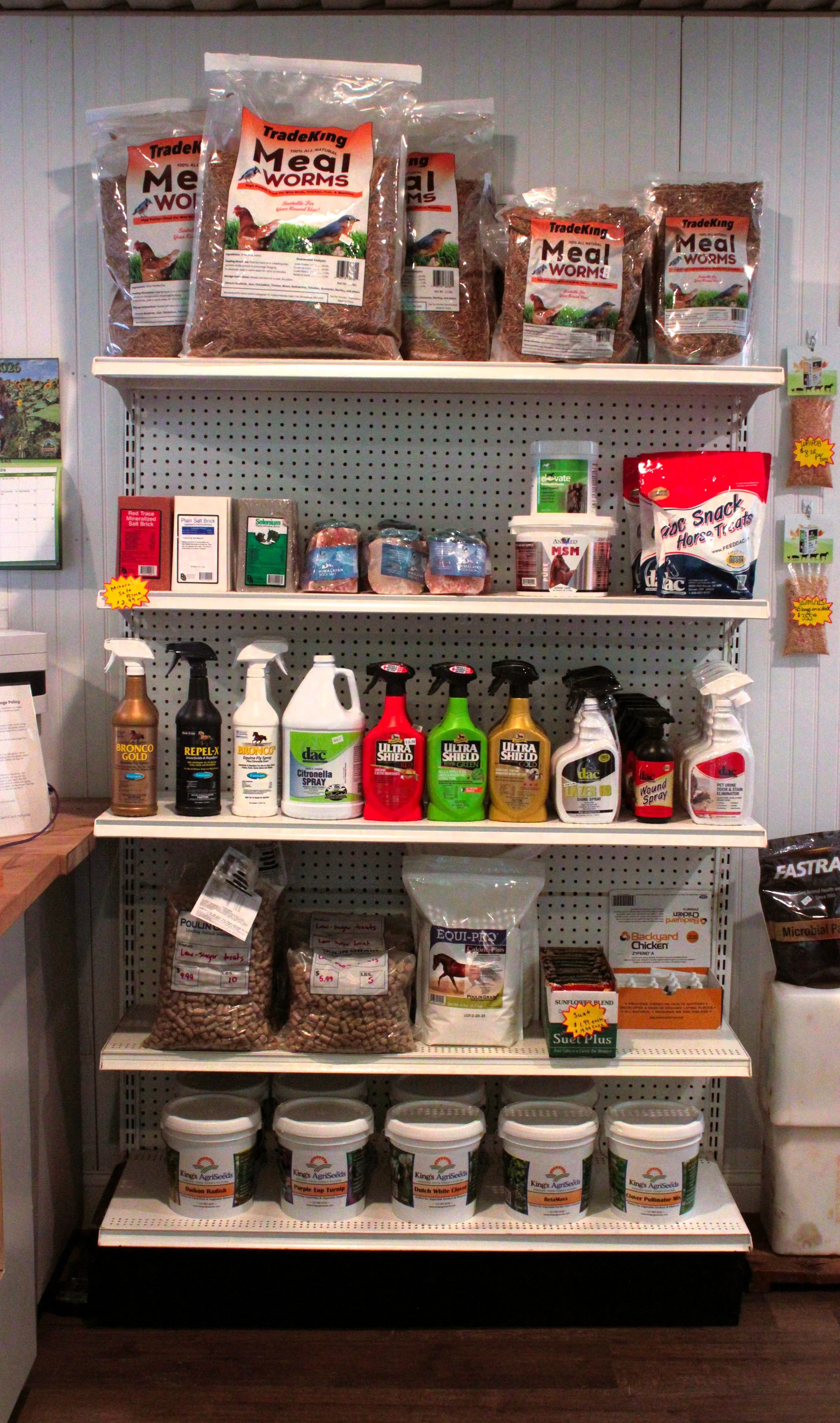 Shelves stocked with bird feed and supplies, including bags of mealworms, seed, spray, and containers for small animals.