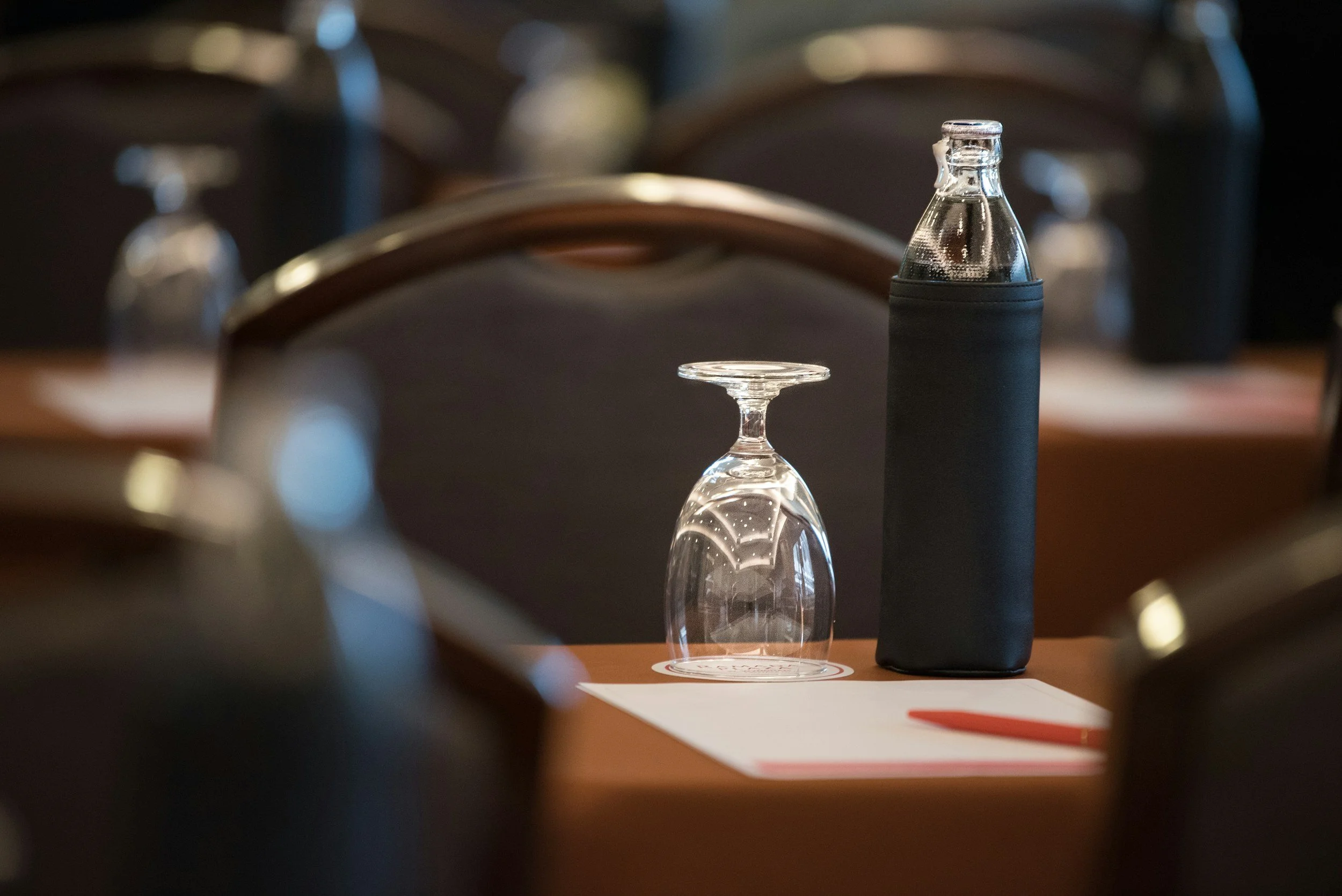 A close up shot of a glass and water bottle, with a notepad and pen.