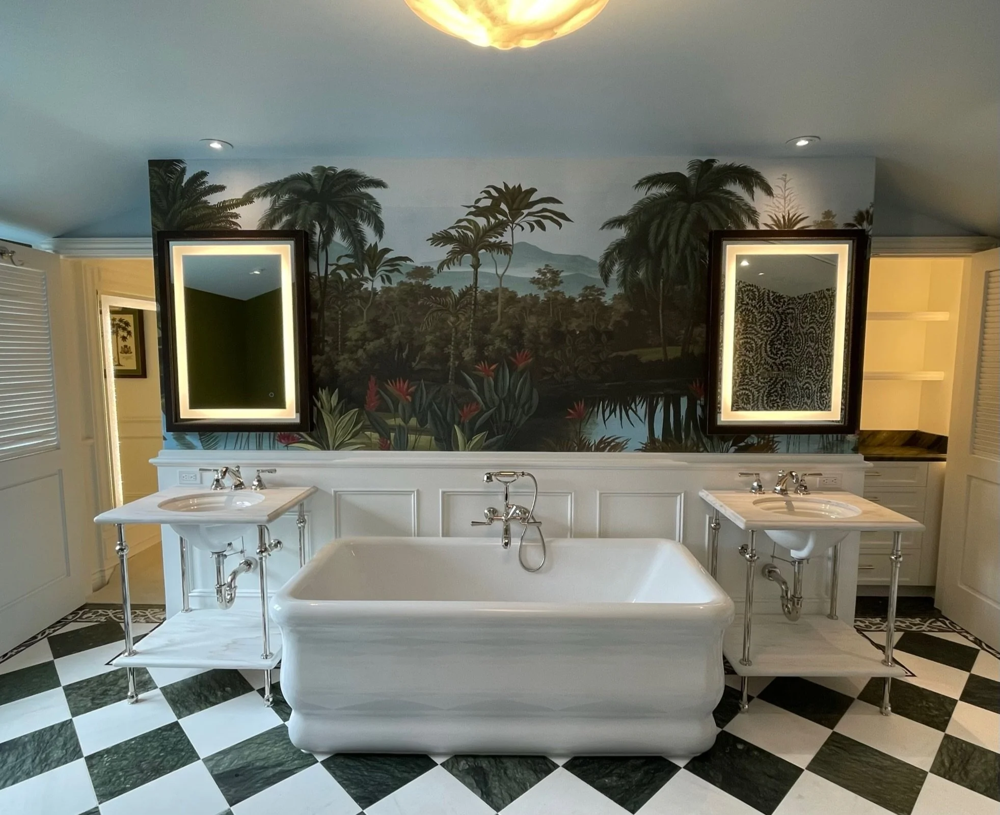 Bathroom with black and white checkered floor, a vintage white bathtub, and two sinks with mirrors above, a jungle mural on the wall, and a gold ceiling light.