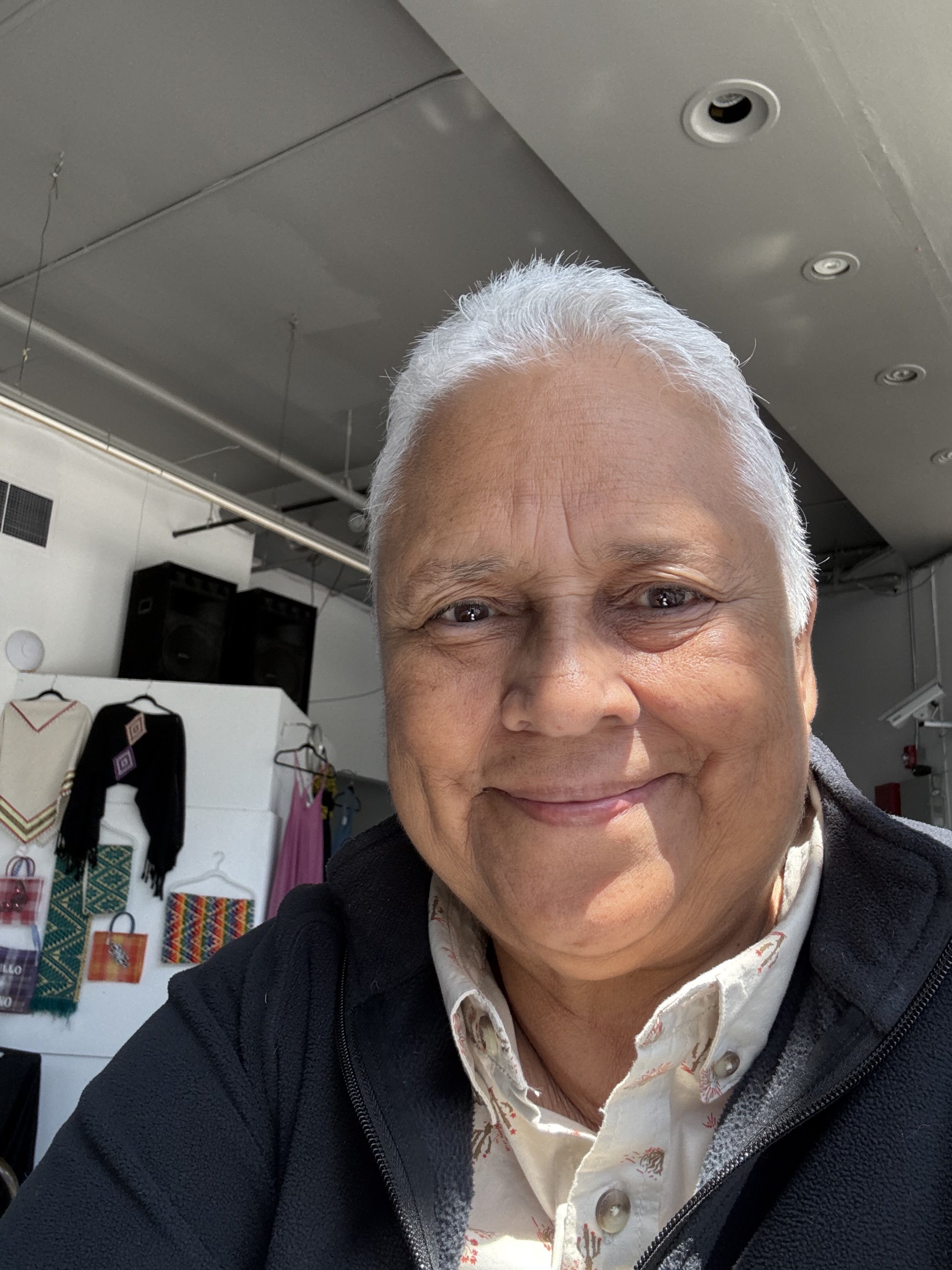 A person with white hair smiling in a room with clothing and decorative items on display in the background.