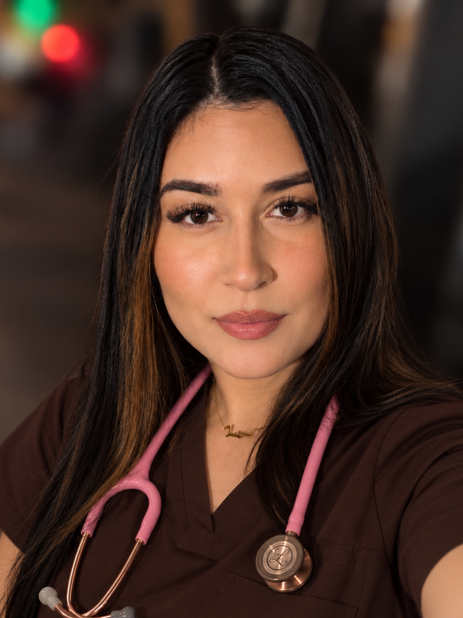 A Latina female nurse wearing a brown uniform with a pink stethoscope around her neck, dark hair, and natural makeup.