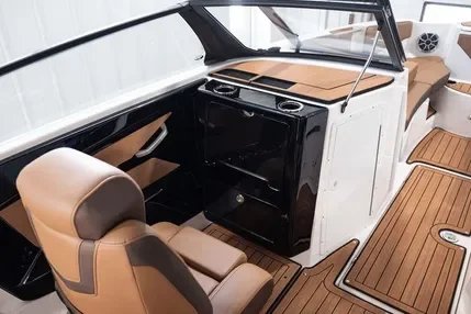 Interior of a boat with tan cushioned seating, a black and white dashboard, and a small black oven or microwave.