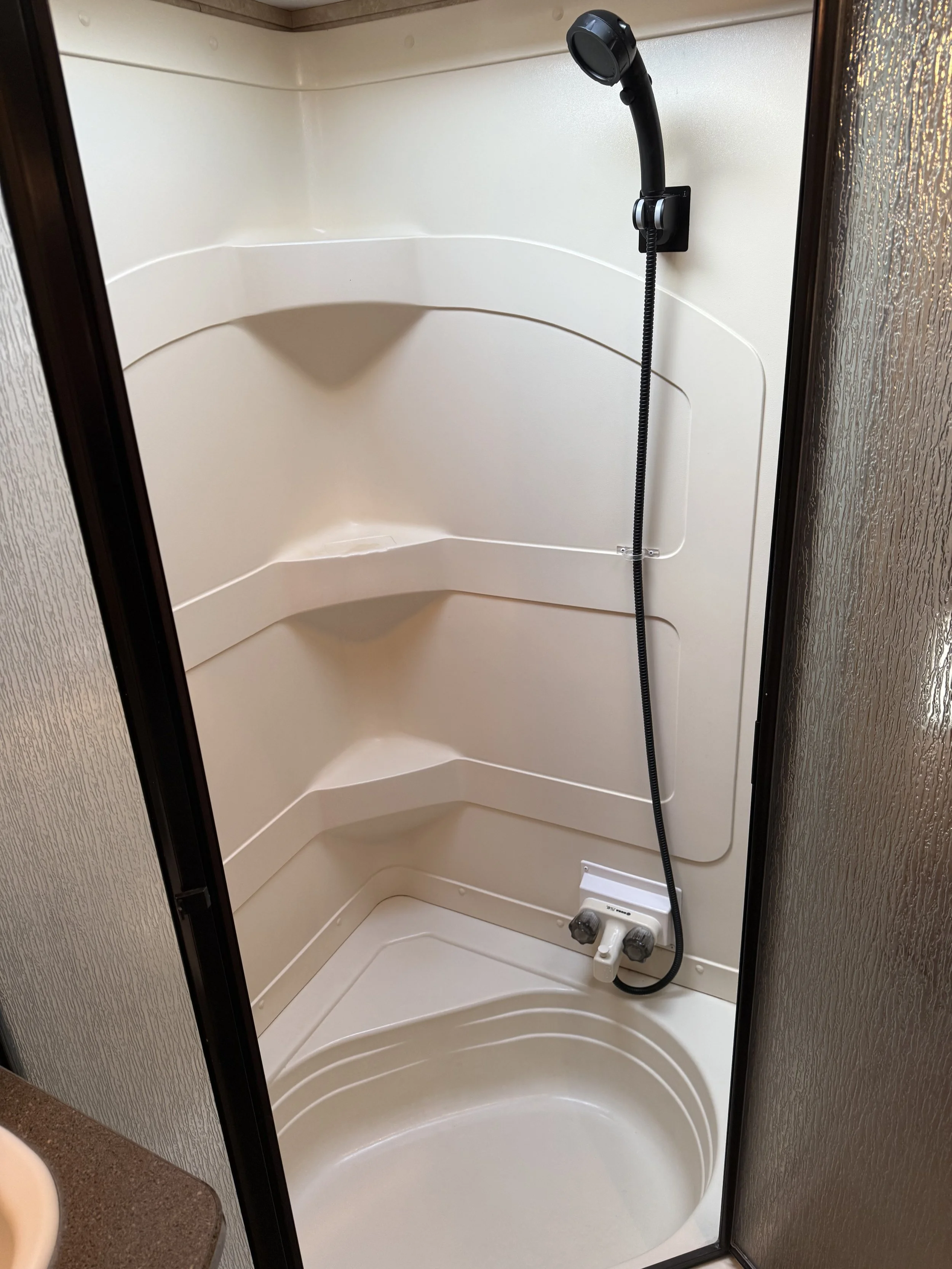 A small shower stall with a black adjustable showerhead, a white control panel, and a built-in seat, enclosed by a sliding door with textured glass.