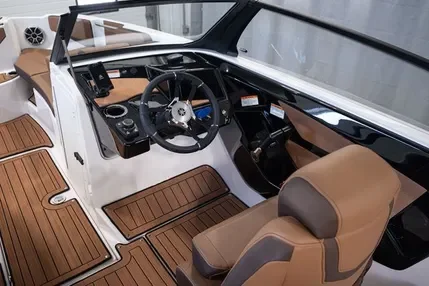 Interior of a boat with a steering wheel, dashboard, and beige cushioned seating with woodgrain flooring.