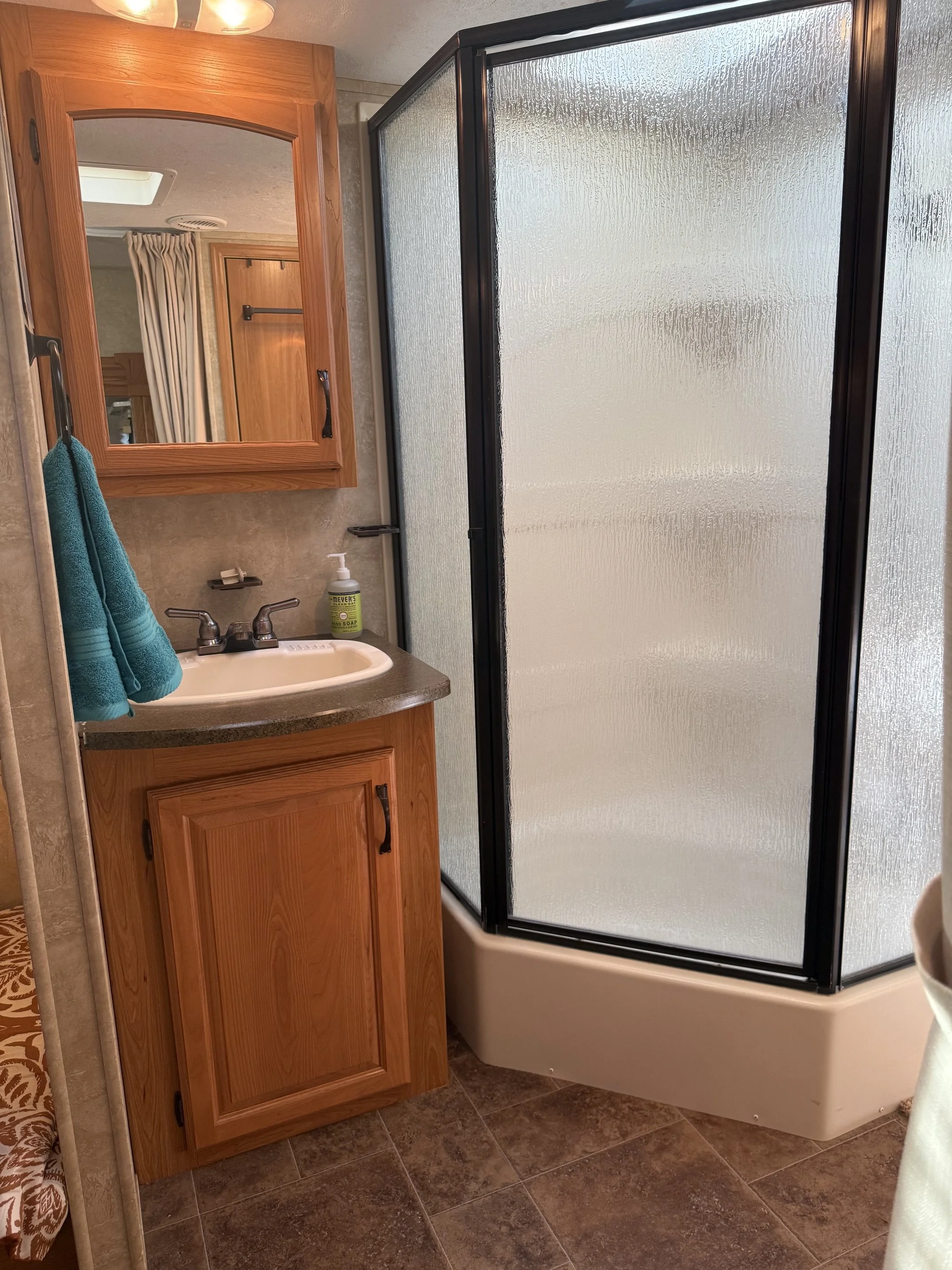 In a bathroom, there is a wooden medicine cabinet with a mirror above the sink, a black shower door, and a bottle of soap on the sink counter.