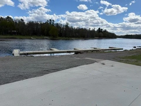 A river with a dock extending into the water, blue sky with clouds, and trees on the far bank.