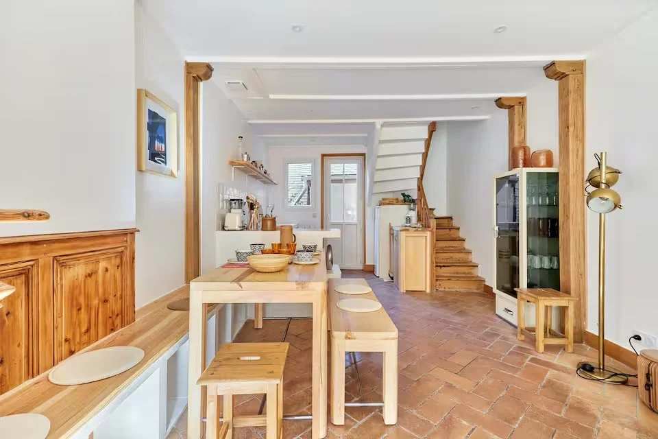 Open-concept kitchen and dining area with wooden accents, white walls, and terracotta tile flooring.