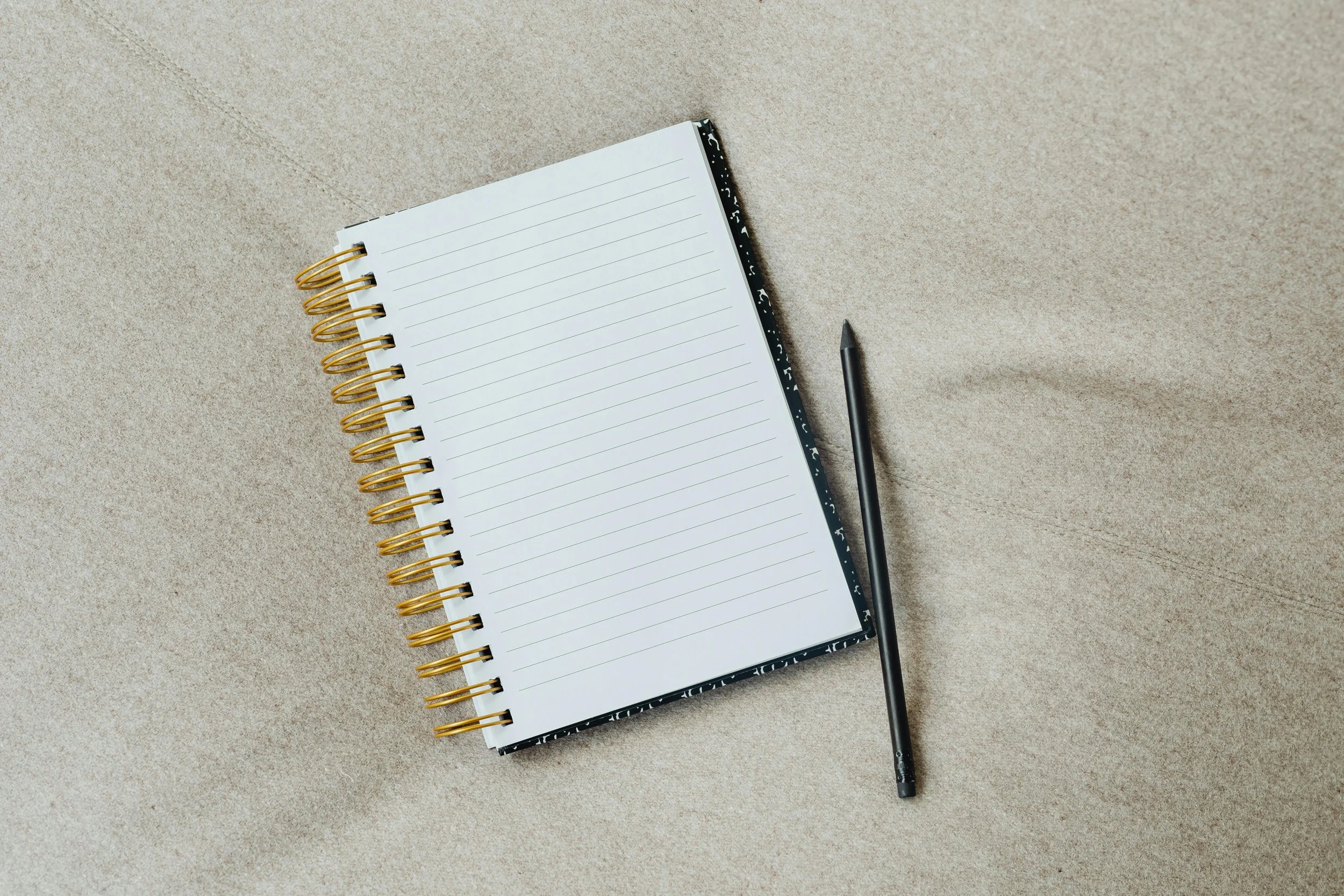 Open spiral notebook with lined pages and a black pen on a tan textured surface.
