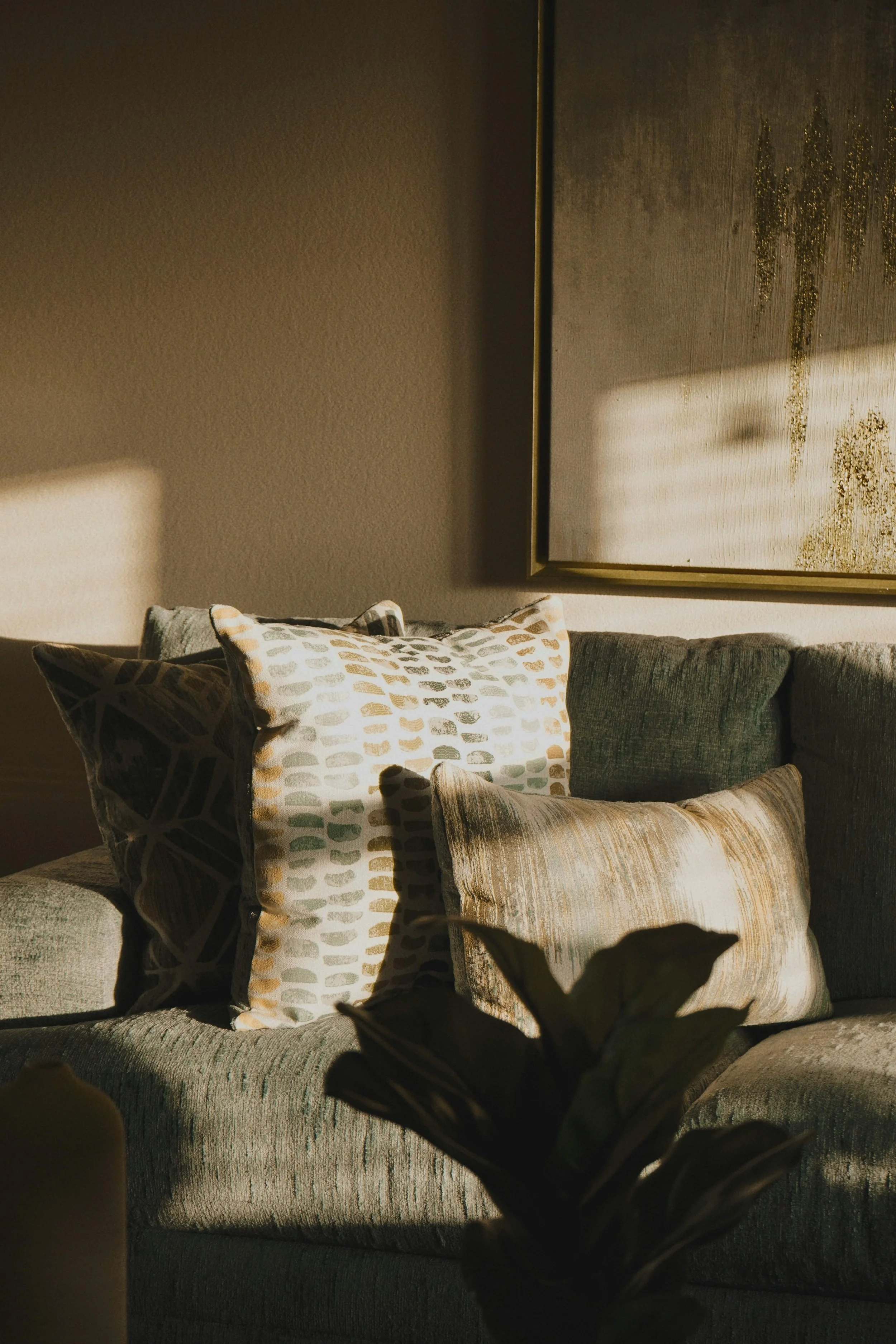 Interior living room with a gray upholstered sofa, decorative pillows, a large abstract framed artwork, and a soft warm lighting creating a cozy atmosphere.