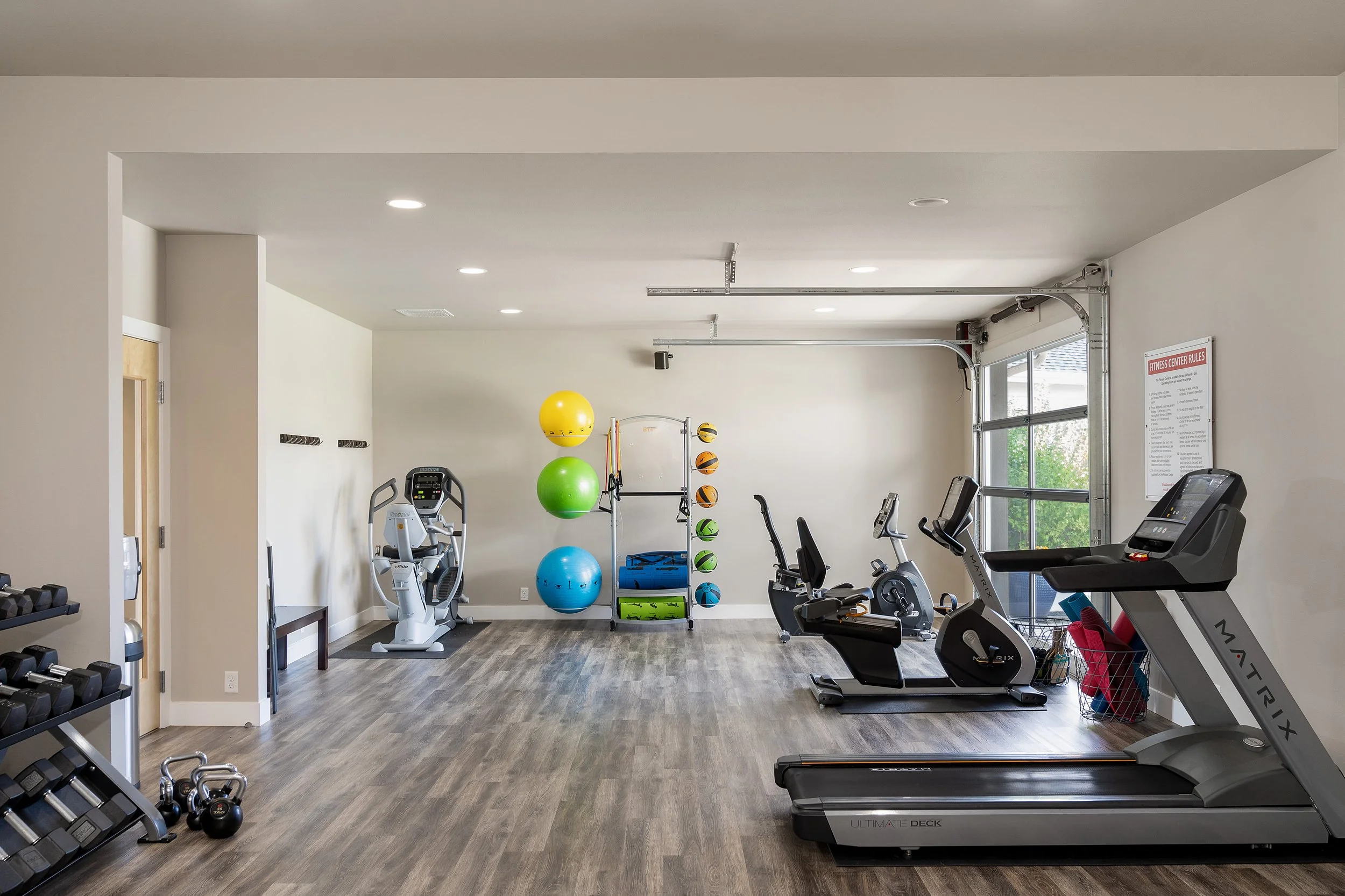 A fitness center with various exercise equipment, including treadmills, stationary bikes, and a rack of colorful exercise balls and weights.
