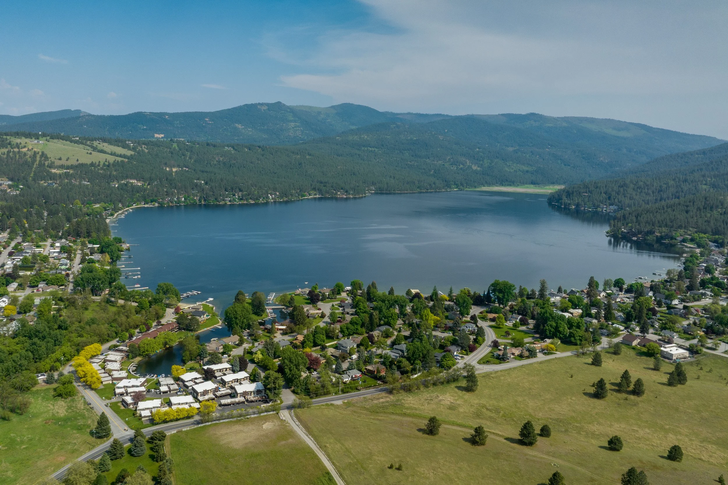 Aerial view of a lake surrounded by lush green hills and a small residential community with houses and trees.