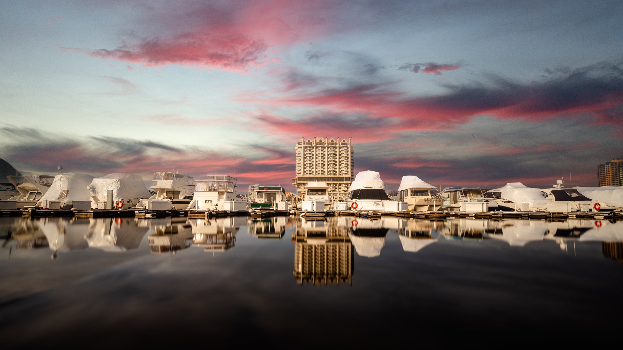 Boats docked at a marina during sunset with a pink and blue sky, reflecting in the calm water.