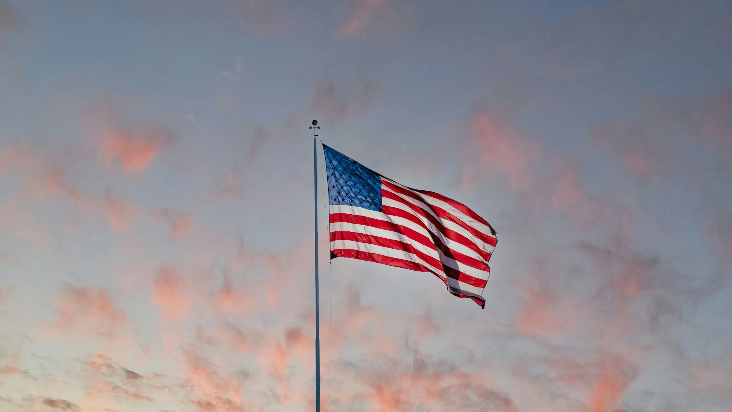 American flag waving in the wind against a sky with pink clouds at sunset