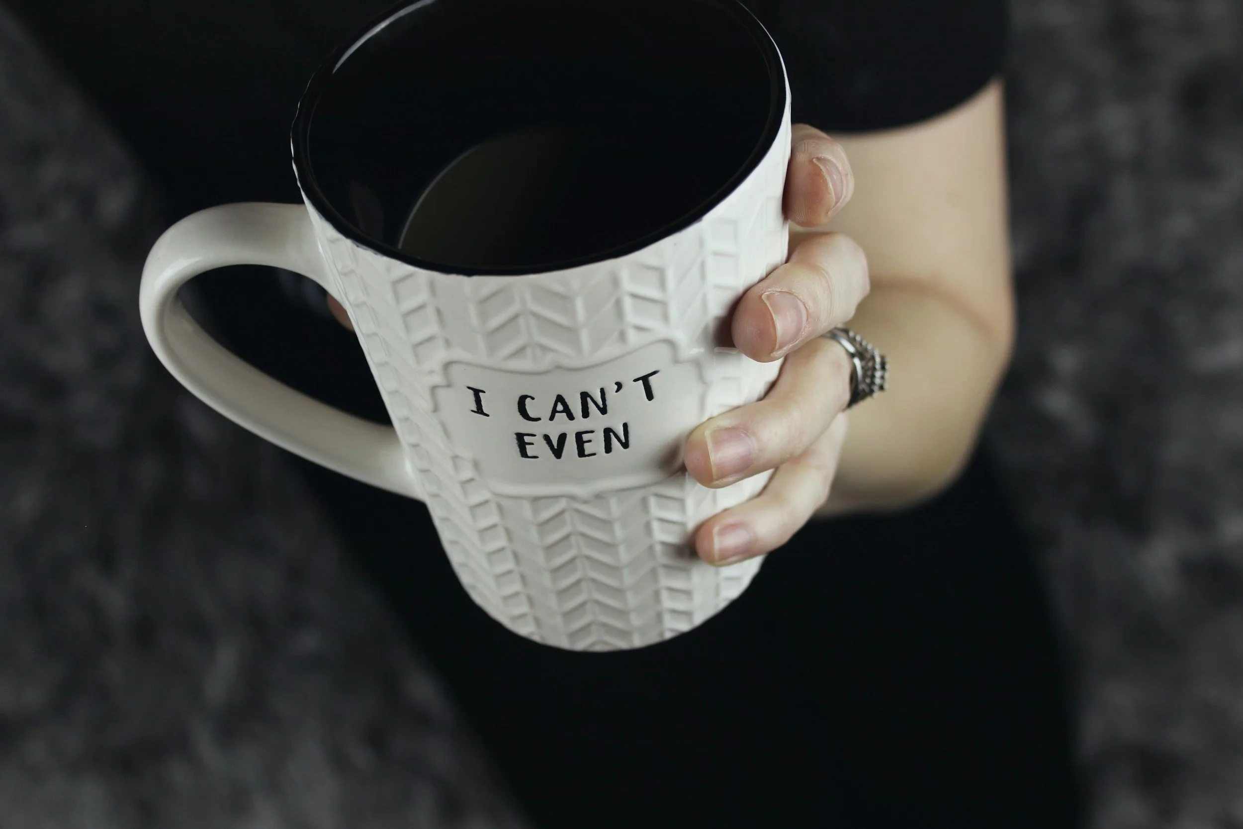 Person holding a white mug with black interior and textured exterior, with the text "I CAN'T EVEN" written on it.