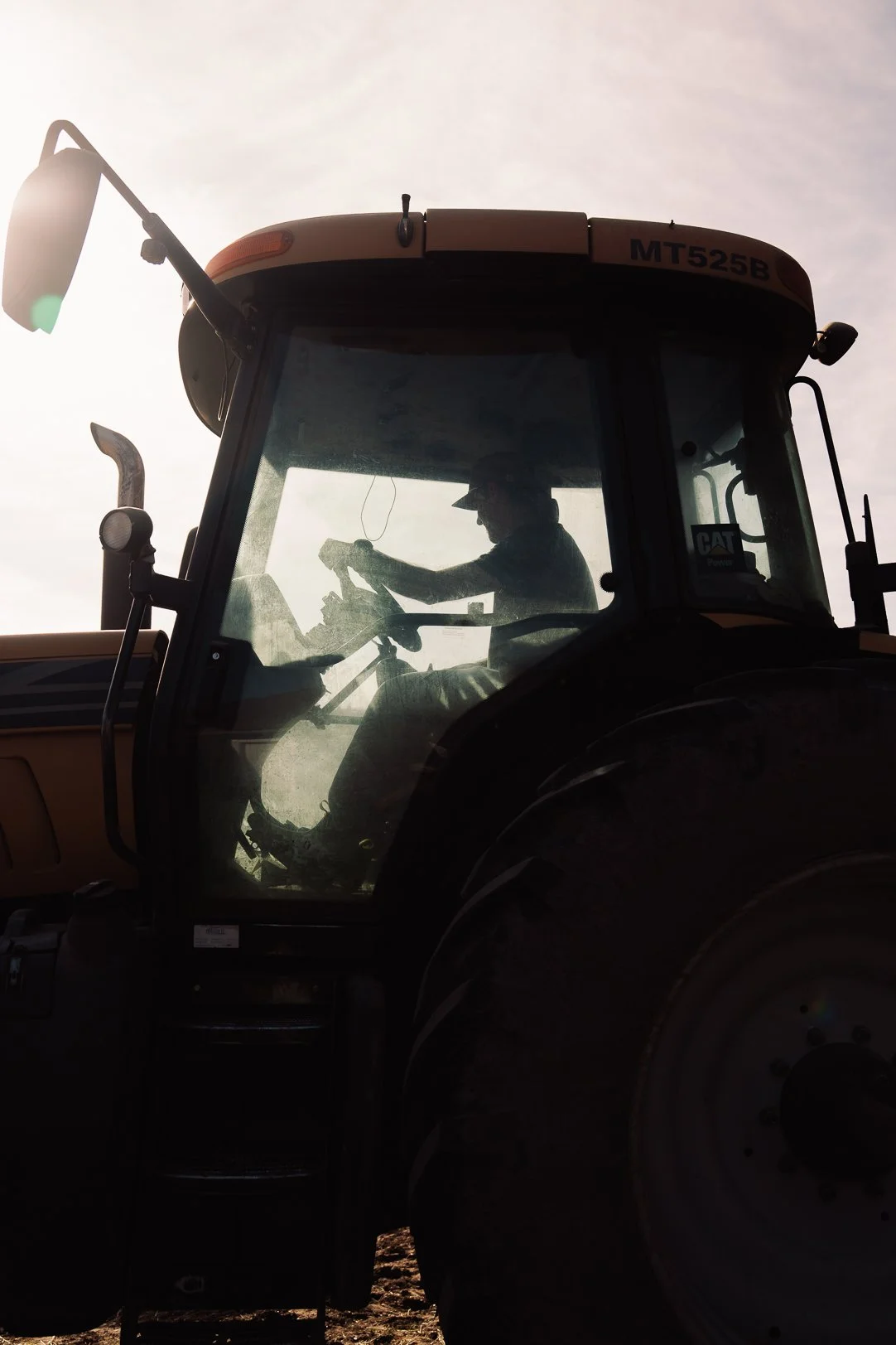 Silhouette of a person operating a large tractor or construction vehicle, with the sun behind, creating a backlit effect.