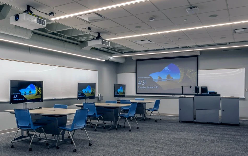 Collaborative learning classroom at Concordia College Integrated Science Center in Moorhead, Minnesota, featuring ceiling-mounted projectors, presentation screens, and group workstations.