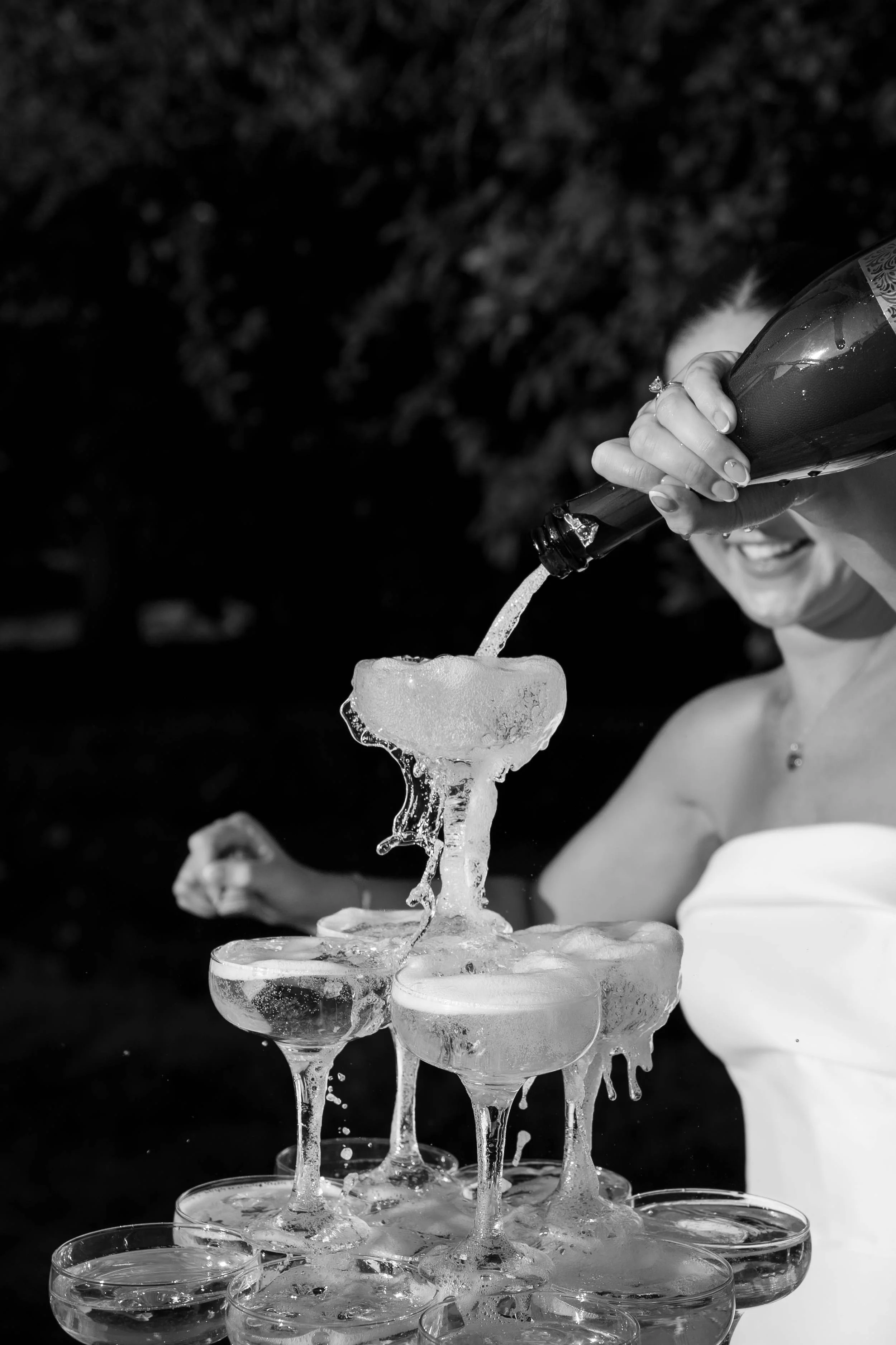 A person pouring champagne into a tower of glasses during a celebration.