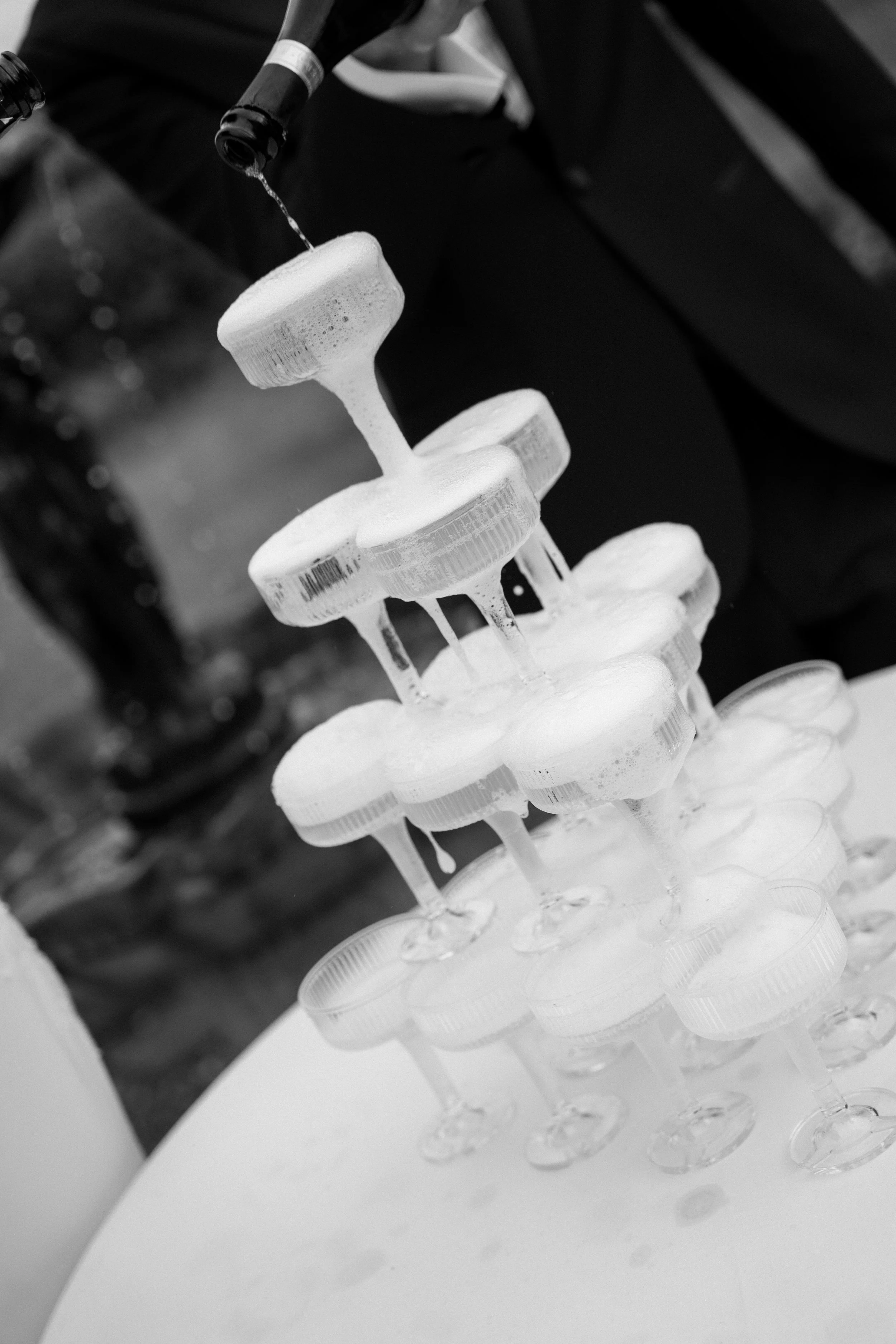 A black-and-white photo of a lab setup with multiple test tubes or containers stacked in a rack, filled with a liquid being poured from a bottle.