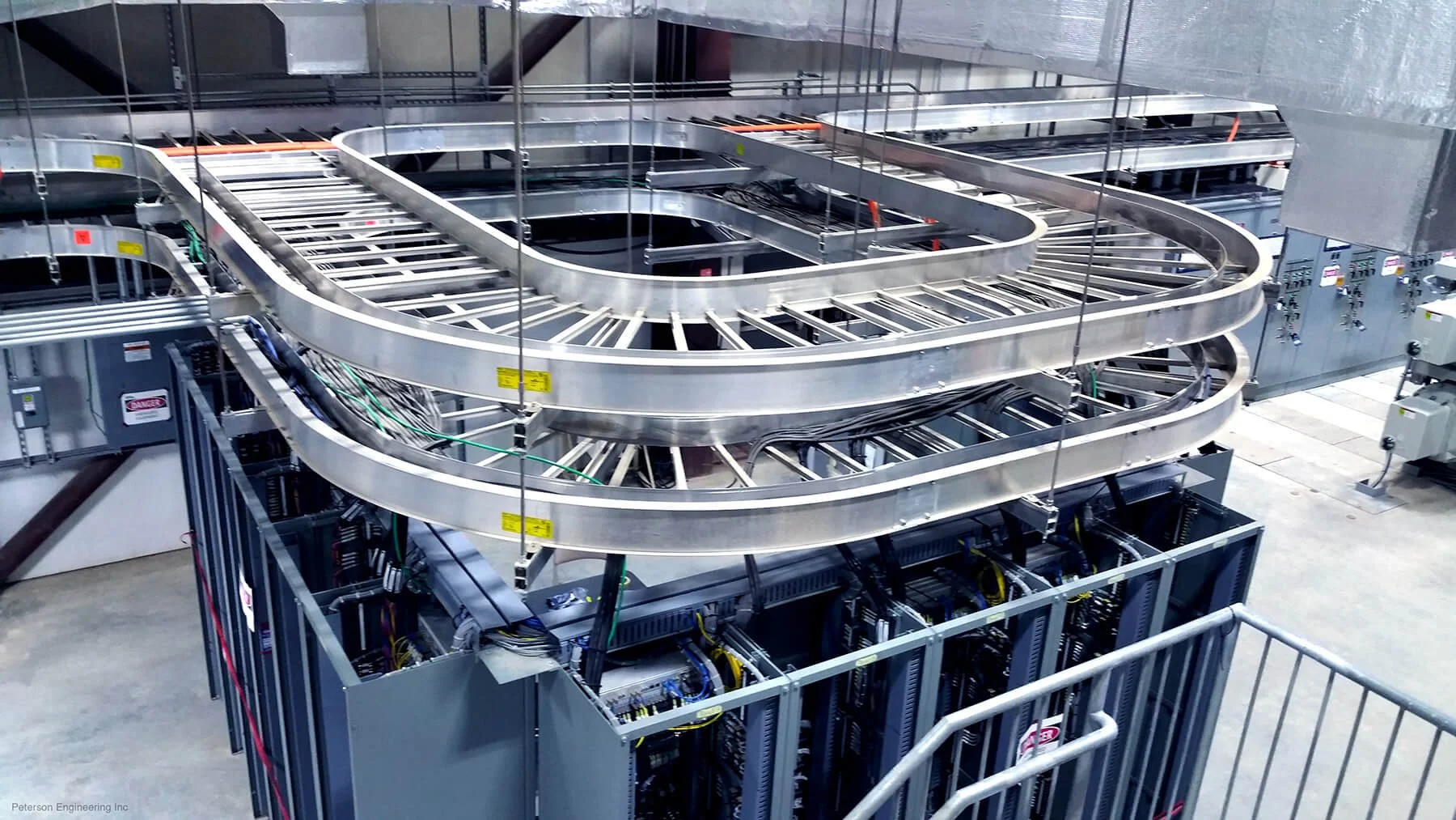 A complex industrial machine with winding metal tracks, electrical wiring, and control panels, located in a manufacturing or data center facility.