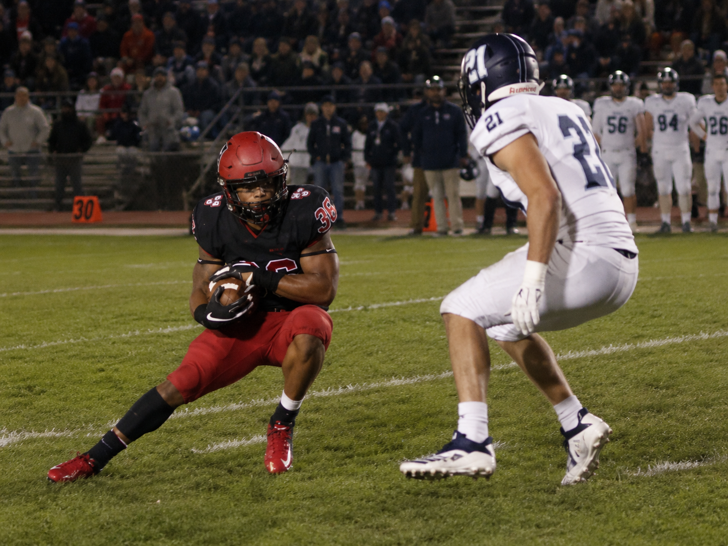 High school football player cutting laterally to evade a defender during a game.