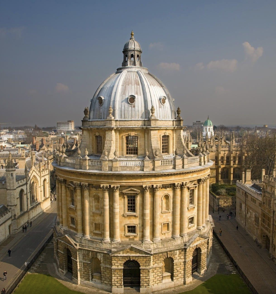 Dome of a historic building with a cityscape in the background, featuring classical architecture and a cloudy sky.