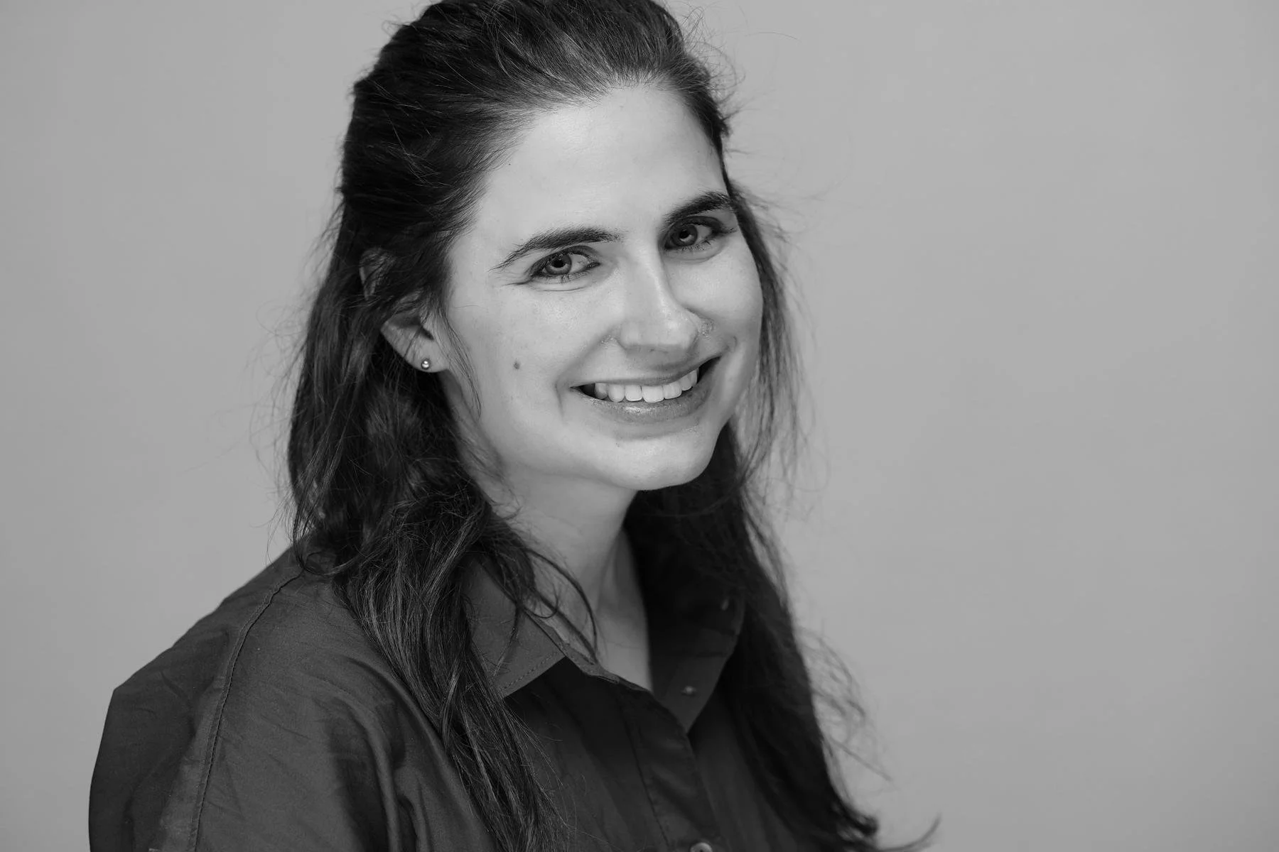 Black and white portrait of a smiling woman with long wavy hair, wearing a dark shirt against a plain background.