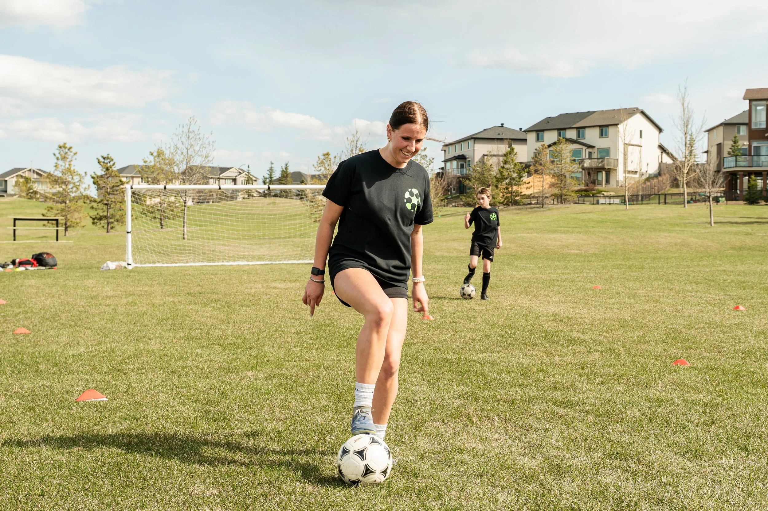 Young soccer player practicing ball control during a youth soccer training session while a coach supervises on a grass field in Calgary.