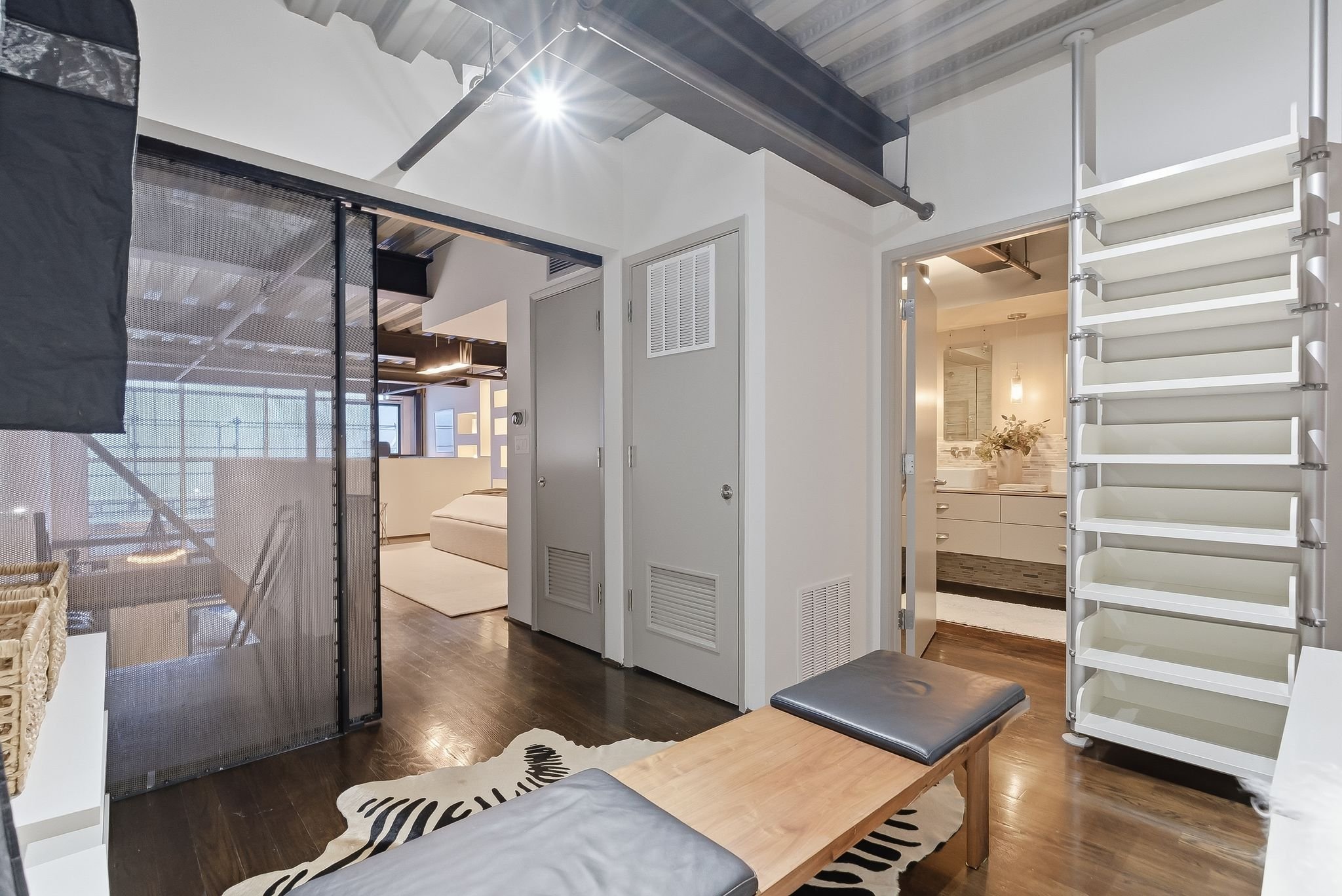 Interior of a modern apartment with a partial view of a bedroom, bathroom, and staircase, featuring neutral colors, wood flooring, and contemporary furniture.