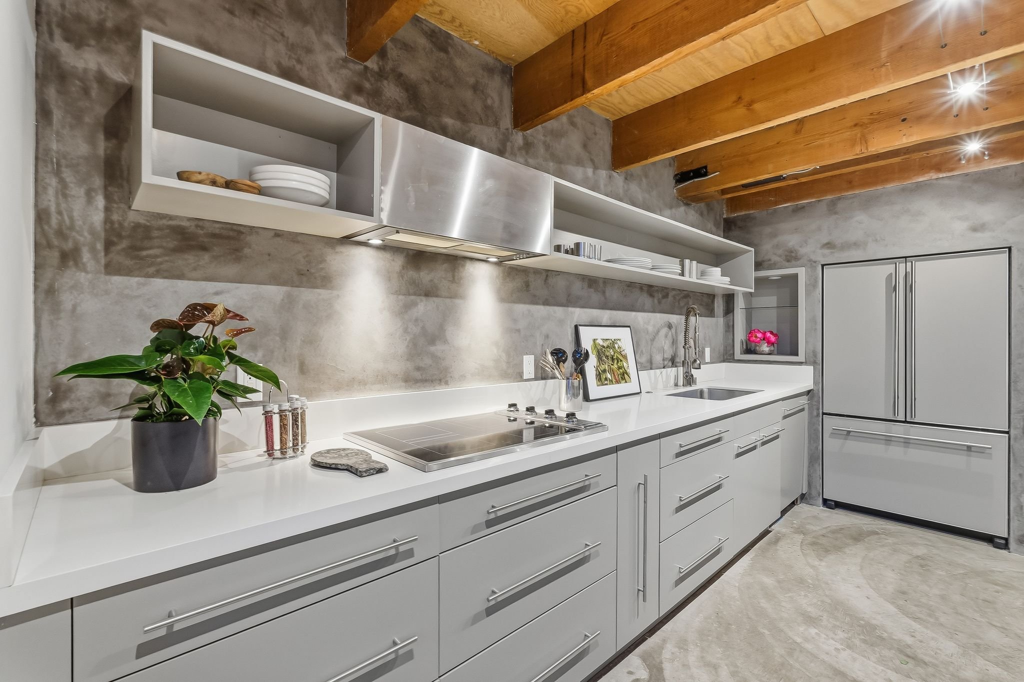 Modern kitchen with white cabinetry, a gray textured backsplash, a stainless steel range hood, and teal ceiling beams. Decor includes potted plants, white plates, and framed artwork.