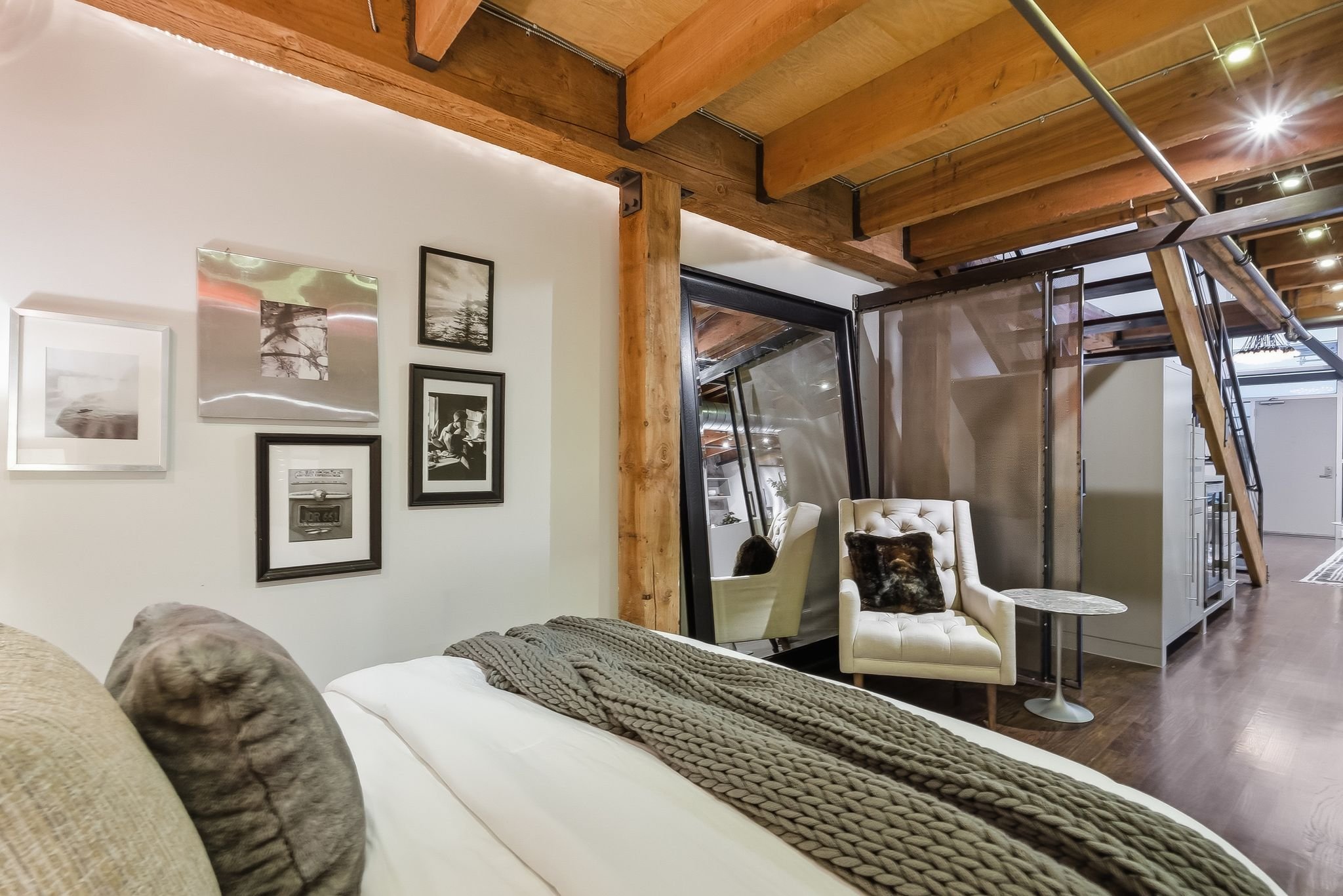 Interior of a modern home featuring a living area with a white sofa, a armchair, and wall art, with excited exposed wooden beams on the ceiling and staircase in the background.