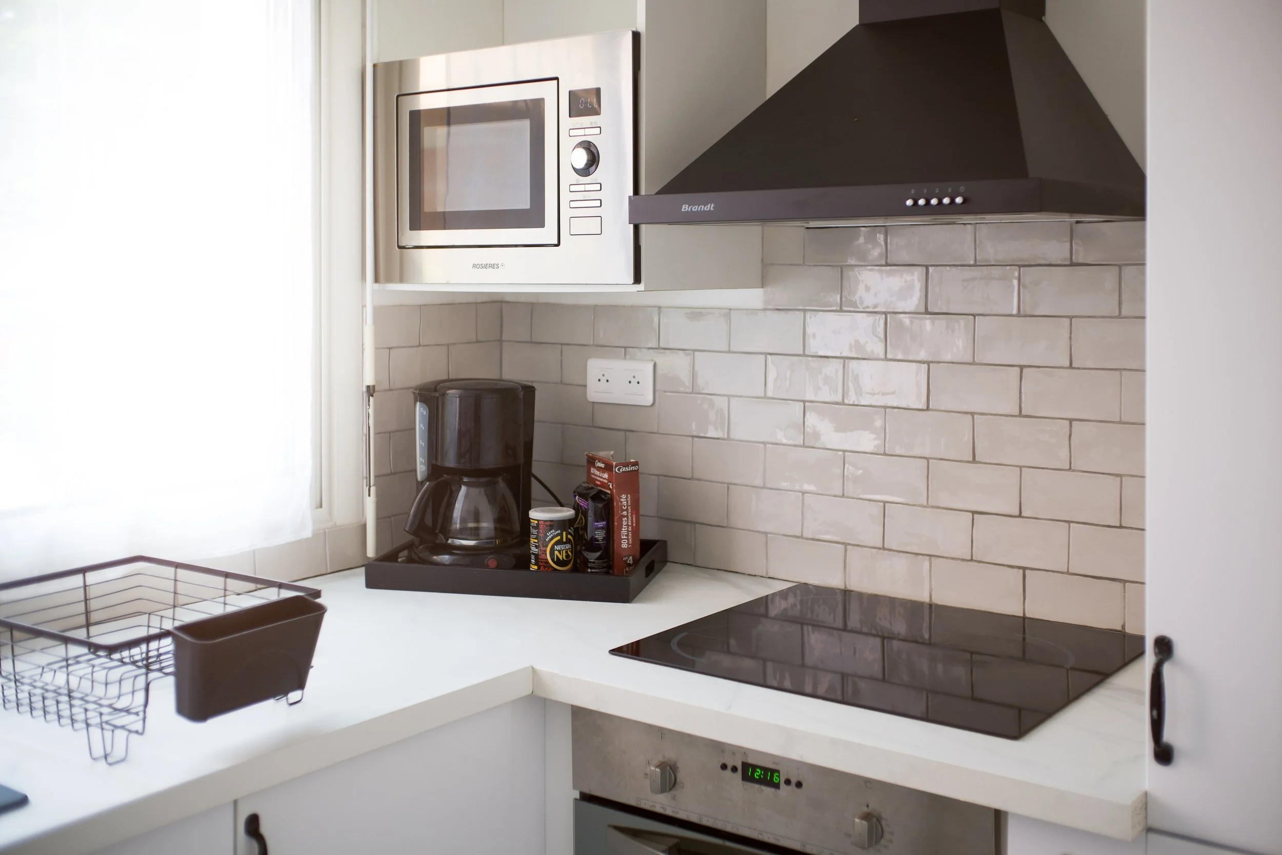 Photographie AirBnB Immobilier. Coin cuisine avec micro-ondes, hotte, plaques électriques, cafetière, tiroir de rangement, et prises électriques sur mur en arrière-plan.